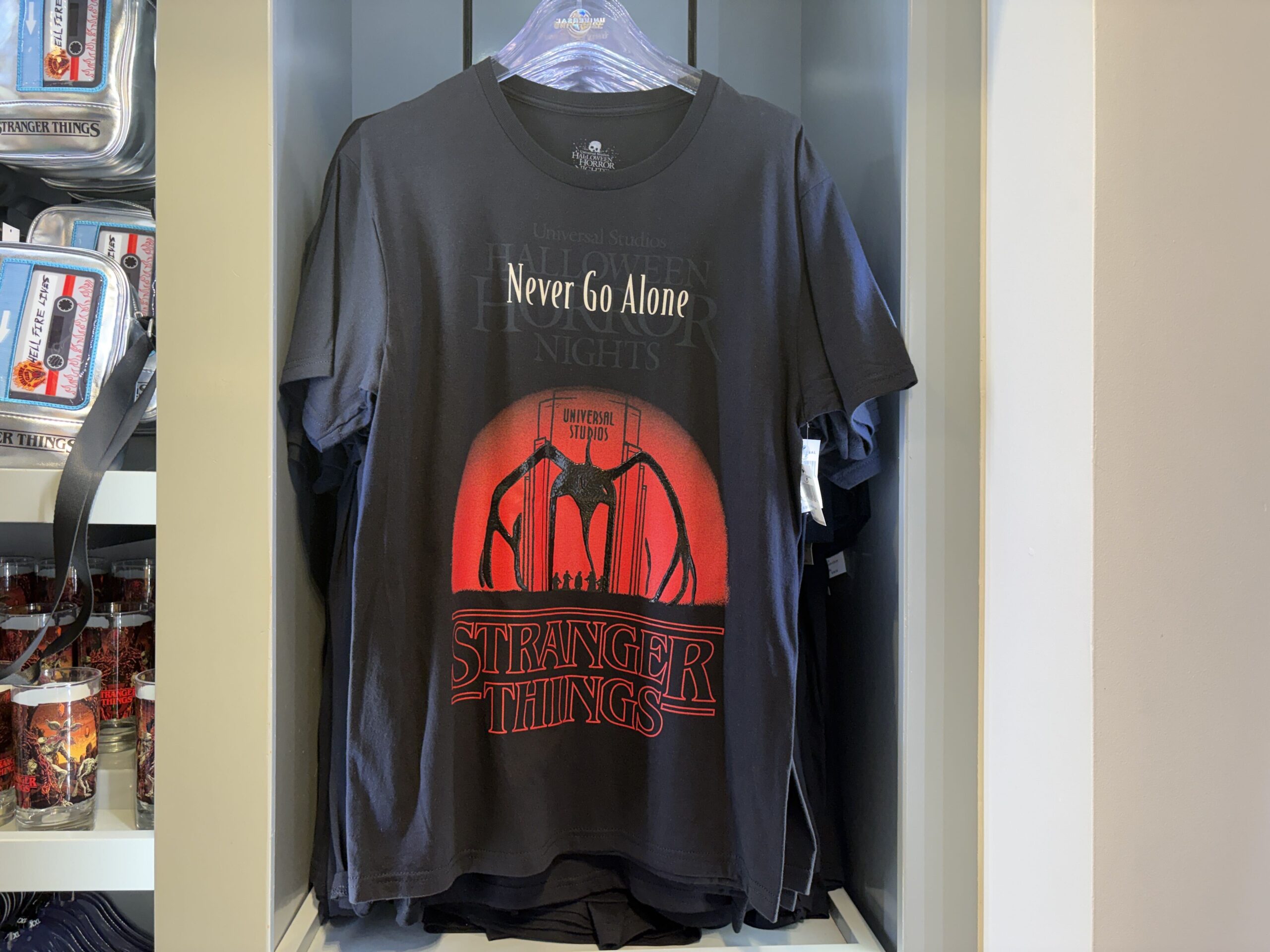 A dark T-shirt on a hanger printed with the Mind Flayer silhouetted inside the Universal Studios archway against a red sun