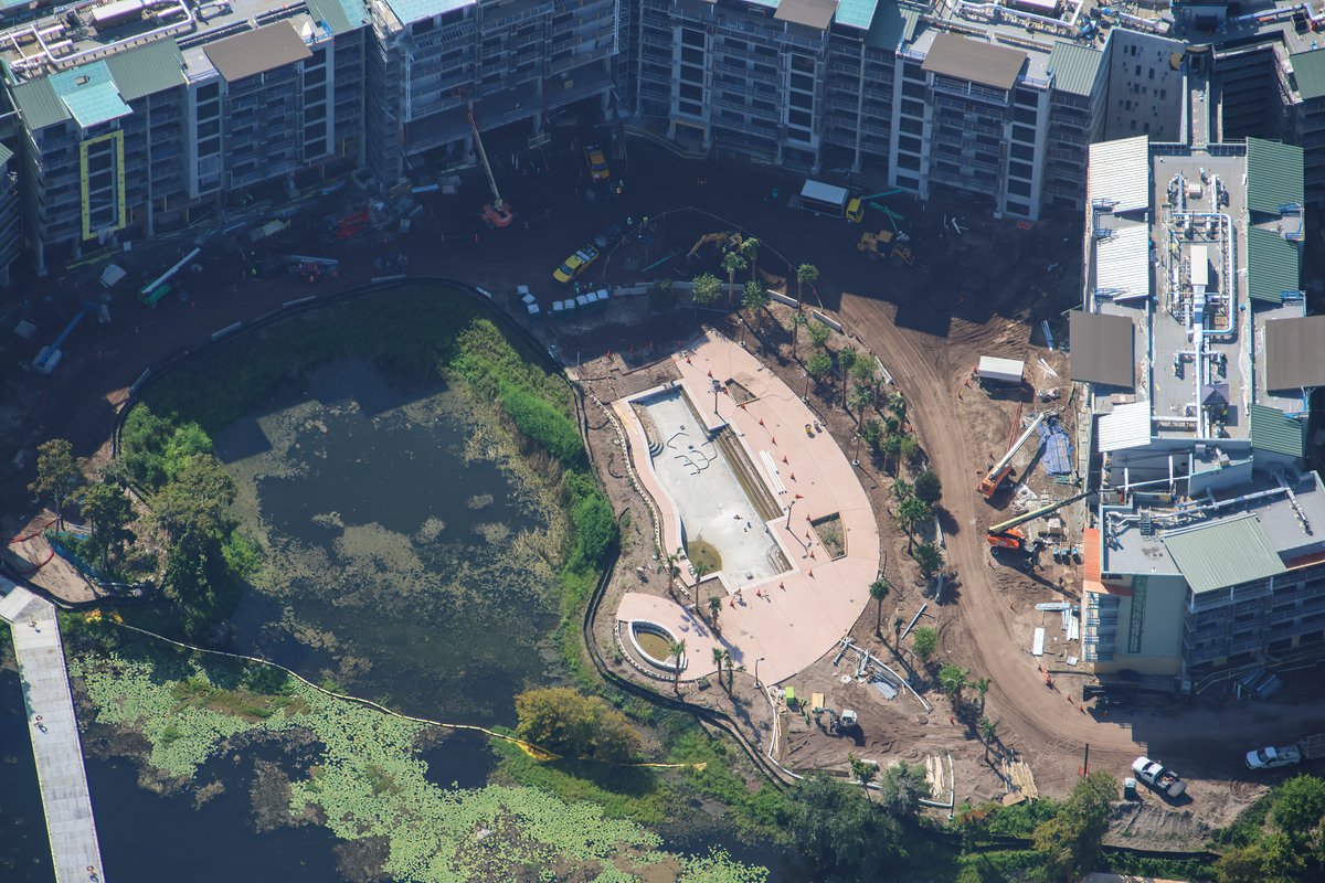 Aerial view of a poured pool shell with pink-tan decking on a cleared peninsula beside a marshy lagoon