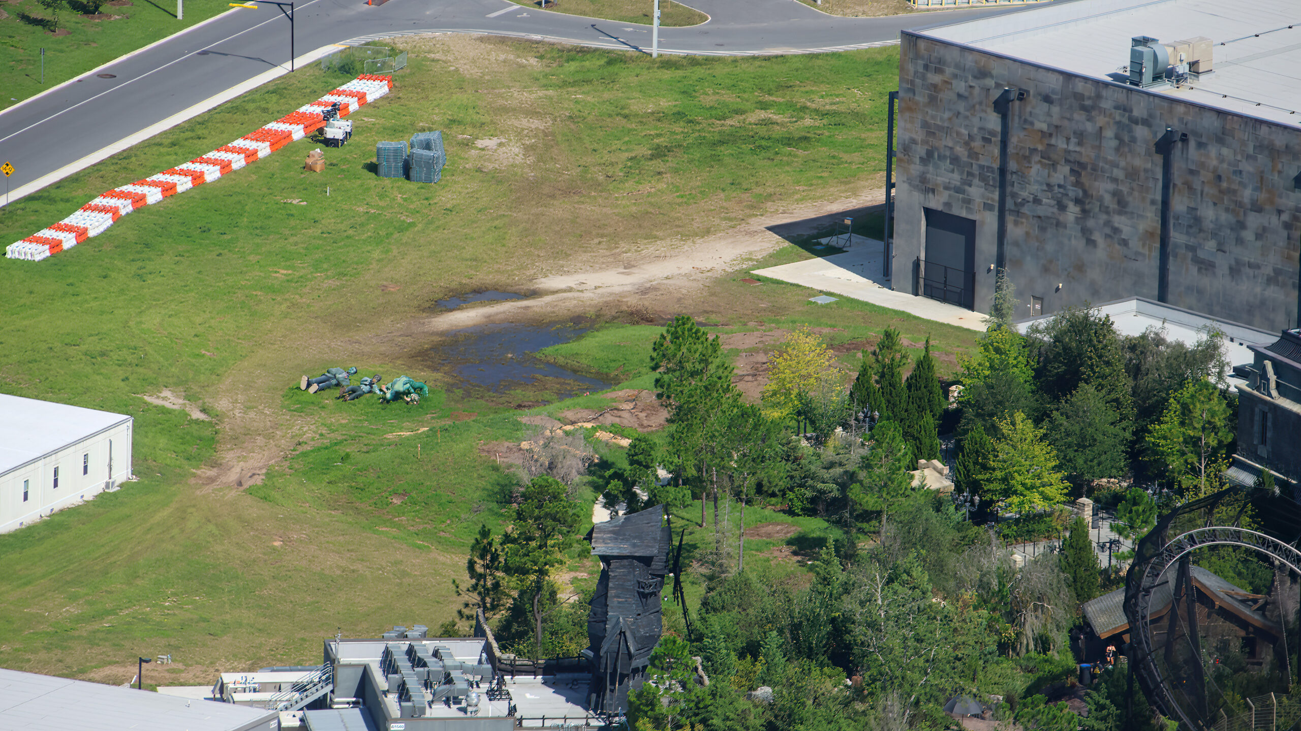 Aerial view of a cleared grass plot behind the stone Monsters Unchained show building, with orange and white barriers along the road