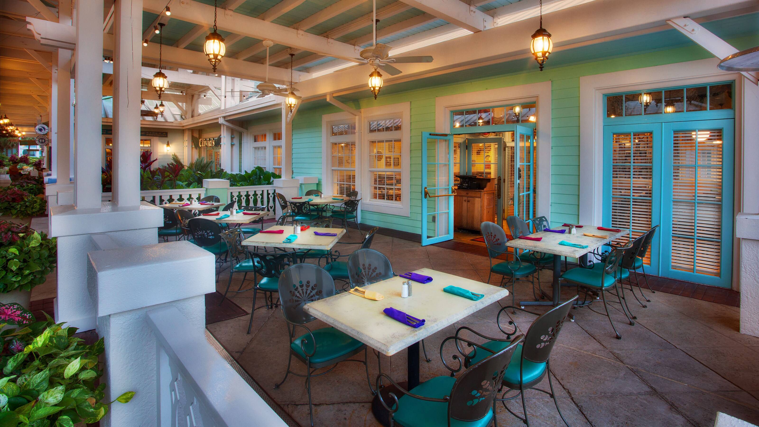 The covered outdoor patio at Olivia's Cafe with teal chairs, stone-topped tables and hanging lantern lights