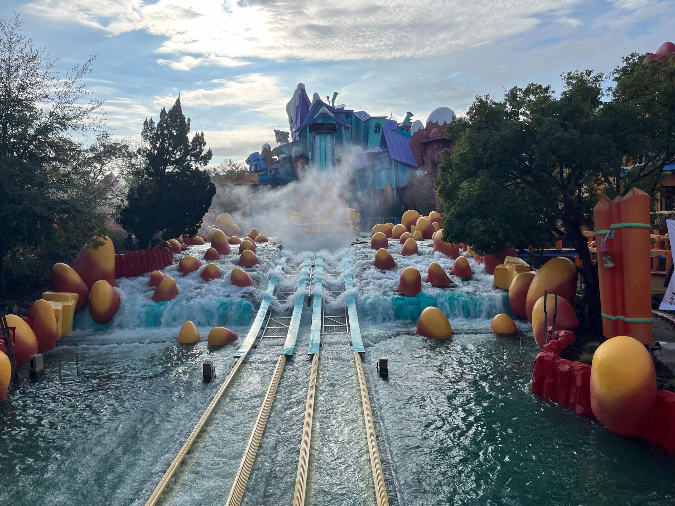The splashdown and flume troughs of Dudley Do-Right's Ripsaw Falls at Islands of Adventure, with water rushing over orange and yellow boulders below a blue and purple cartoon lodge