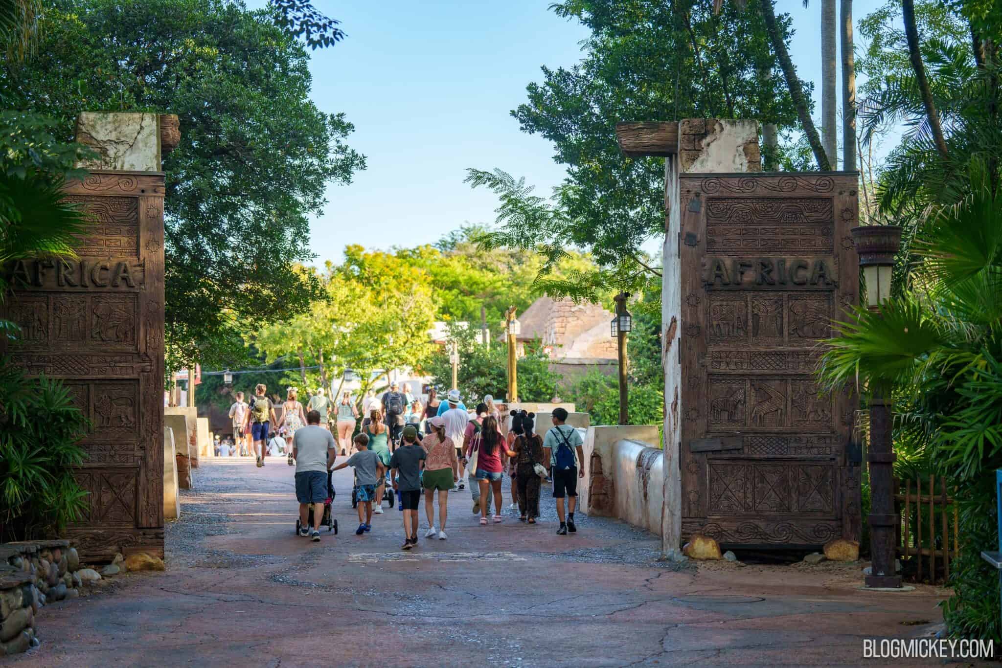 The Africa land entrance at Animal Kingdom, two tall carved wooden doors with AFRICA carved across each one, guests walking away from the camera on reddish paving