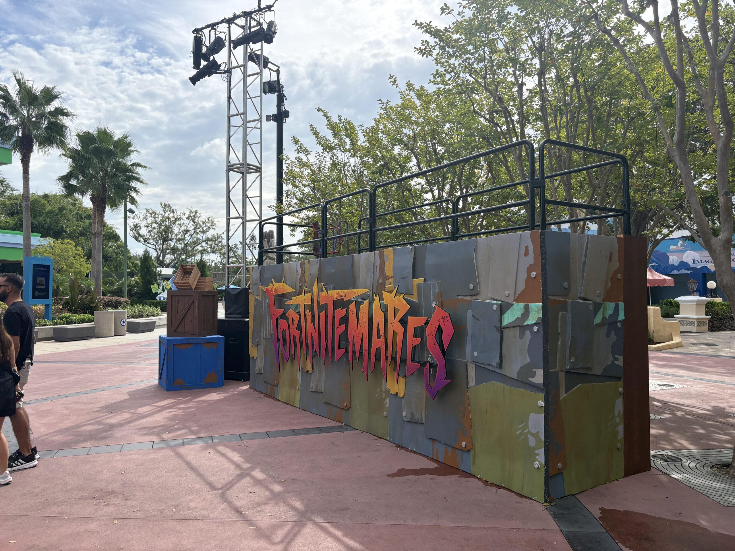 A wall of weathered bolted metal plates carrying the word FORTNITEMARES in jagged letters that shade from yellow through orange to hot pink