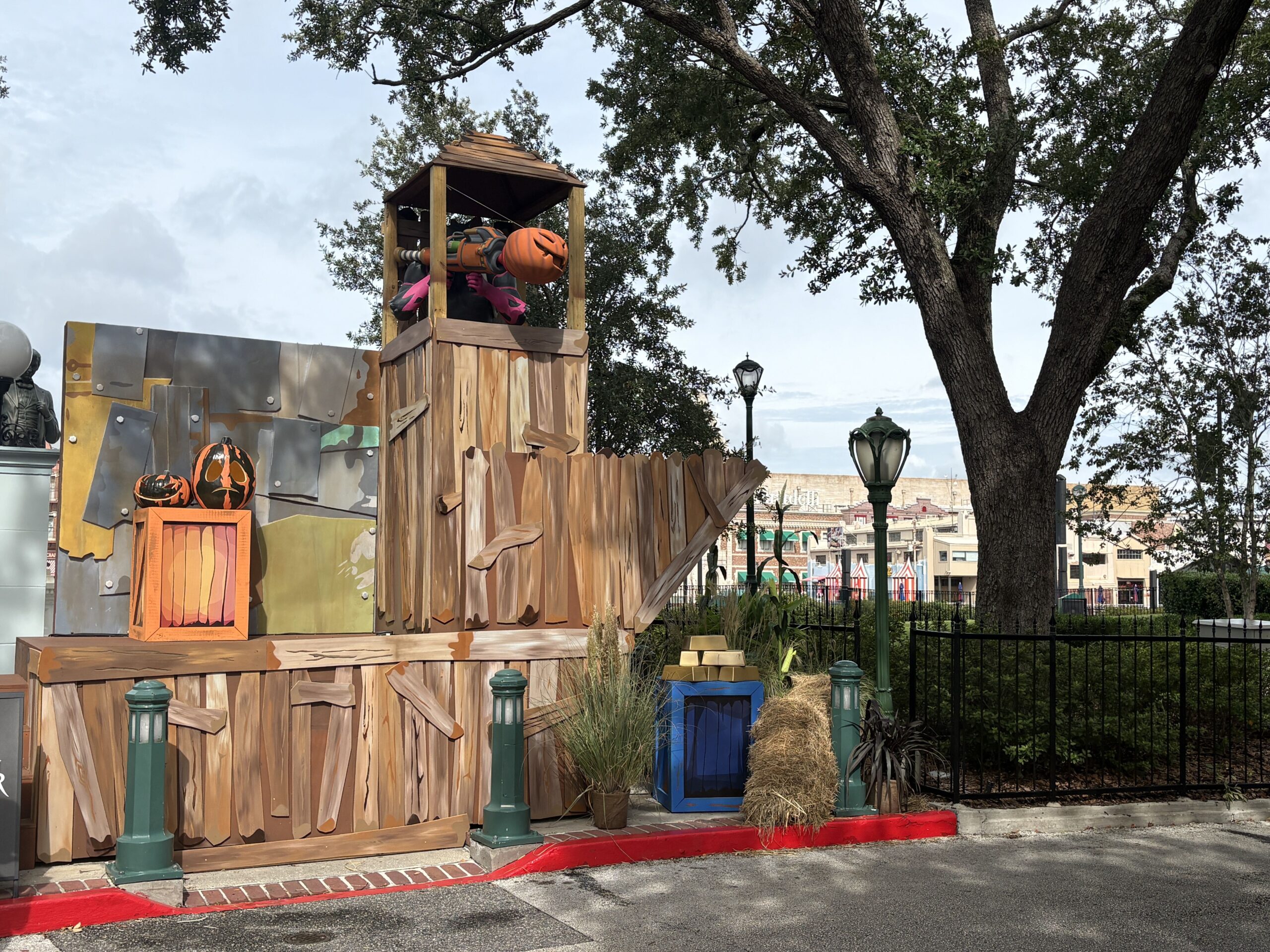 A wooden player built fort with a raised lookout tower holding a figure in magenta gloves aiming a launcher tipped with a grinning orange pumpkin