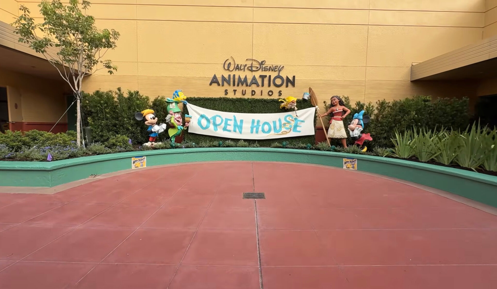 A wide view of the plaza in front of the Open House banner, with a green curved planter wall, a reddish paved plaza and two small Wet Paint signs