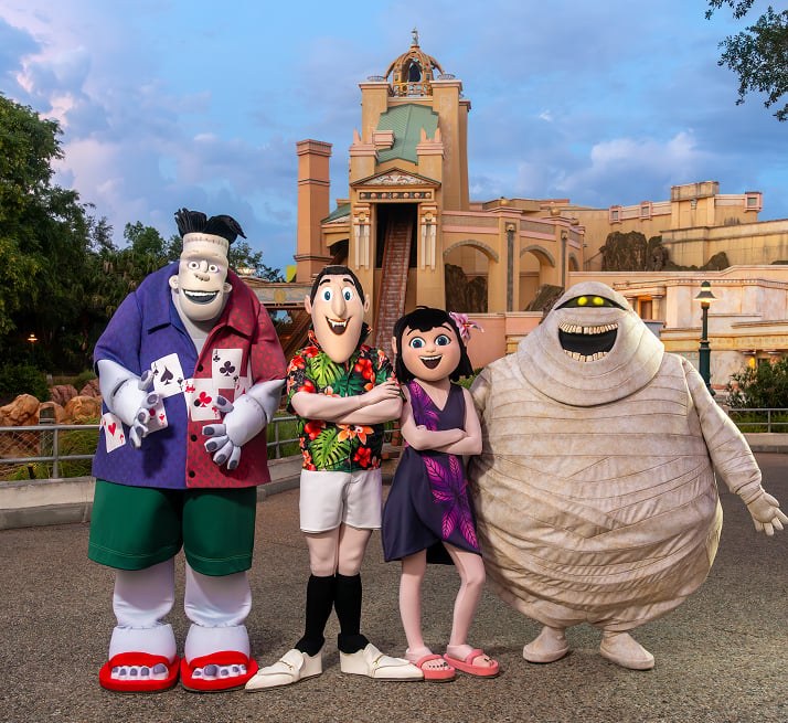 Frankenstein, Johnny, Mavis and Murray the mummy standing together in front of an ornate SeaWorld building at dusk