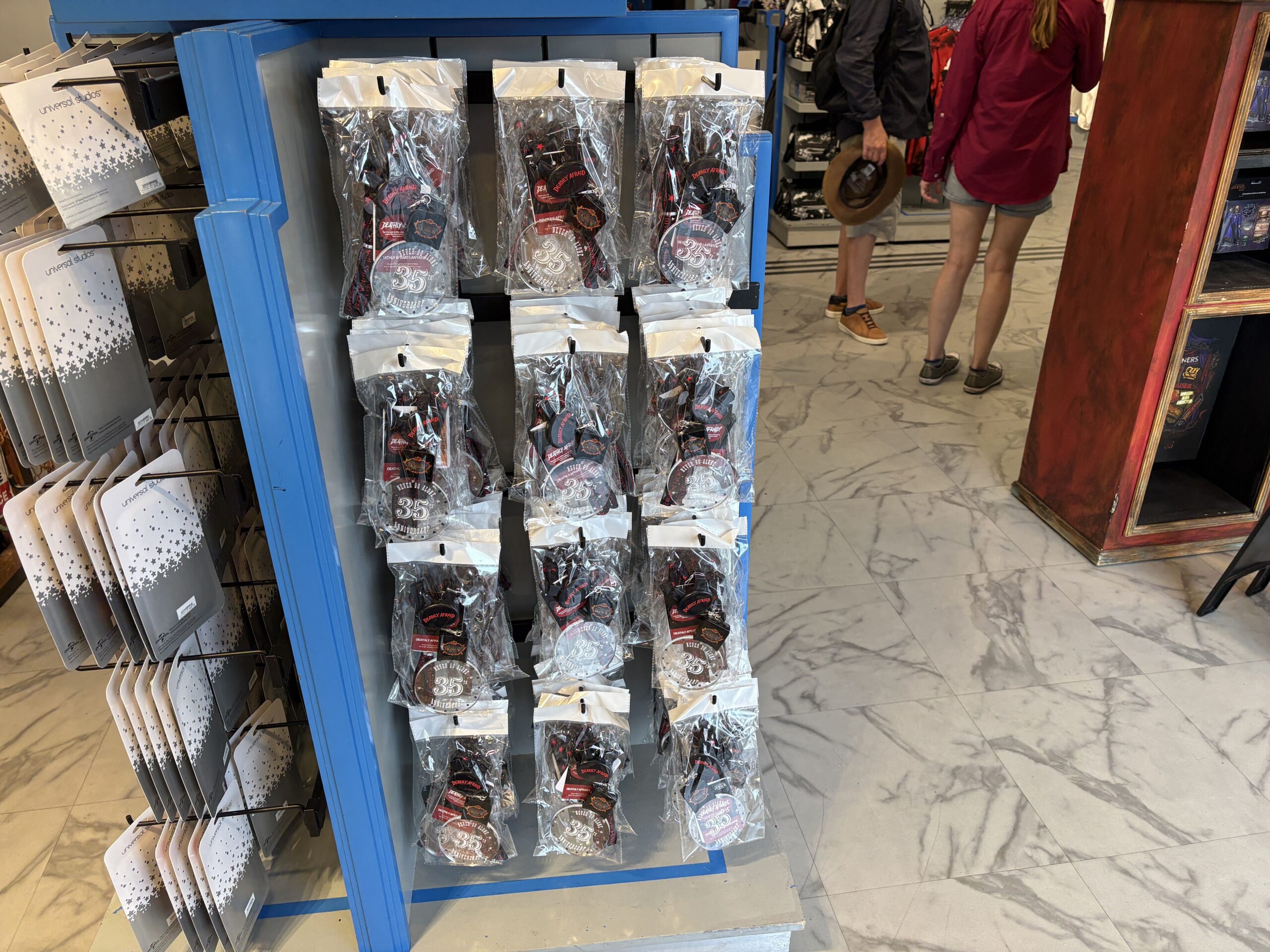 A blue framed retail display rack hung with rows of packaged Deathly Afraid necklaces in clear bags, each showing a 35th Anniversary disc, inside a Universal Studios shop