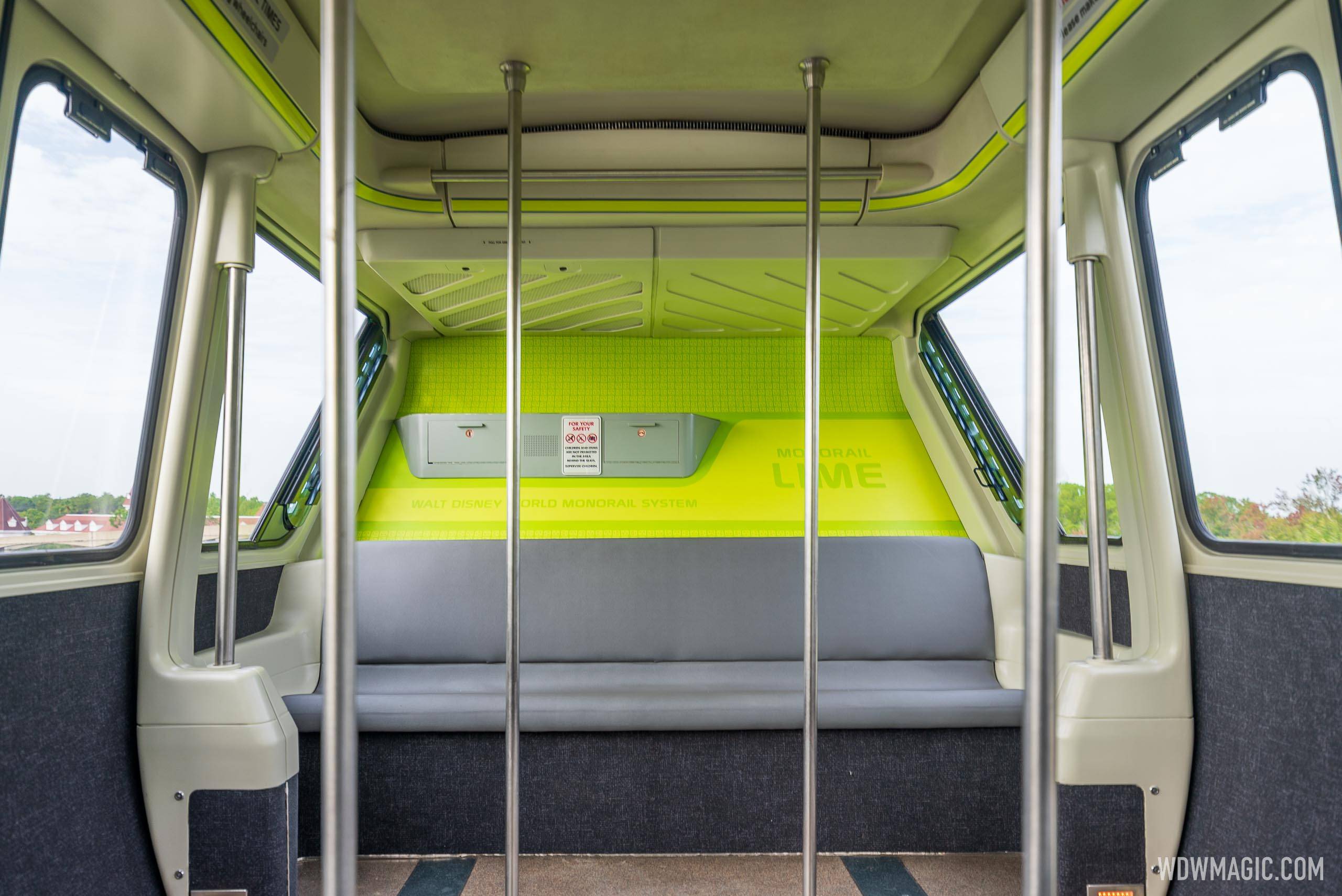 The interior of a Walt Disney World monorail cabin, with grab poles, a grey bench seat and a bright lime green wall panel reading Monorail Lime and Walt Disney World Monorail System