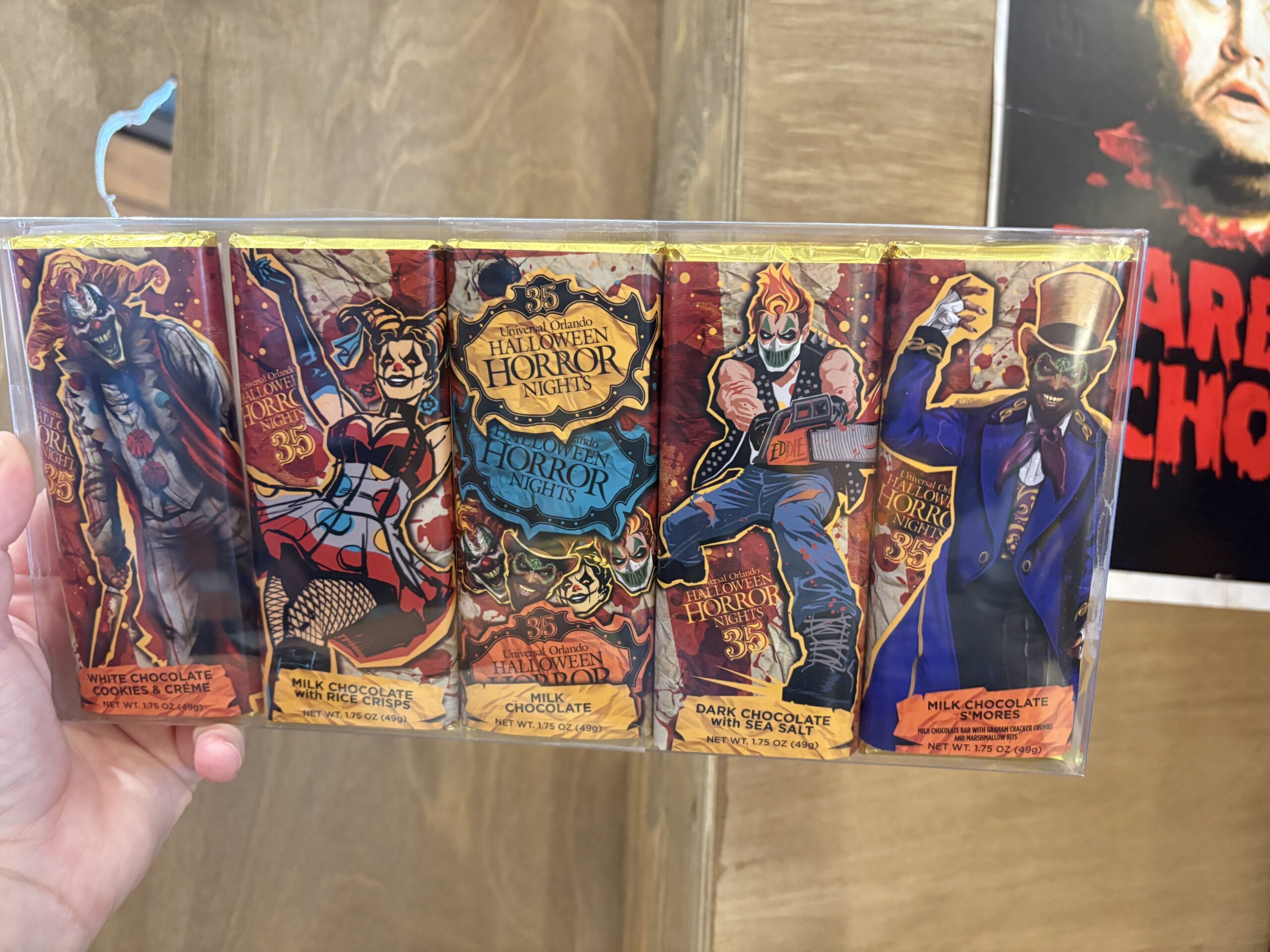 A hand holding a clear boxed set of five Halloween Horror Nights 35 chocolate bars with icon artwork and printed flavor panels