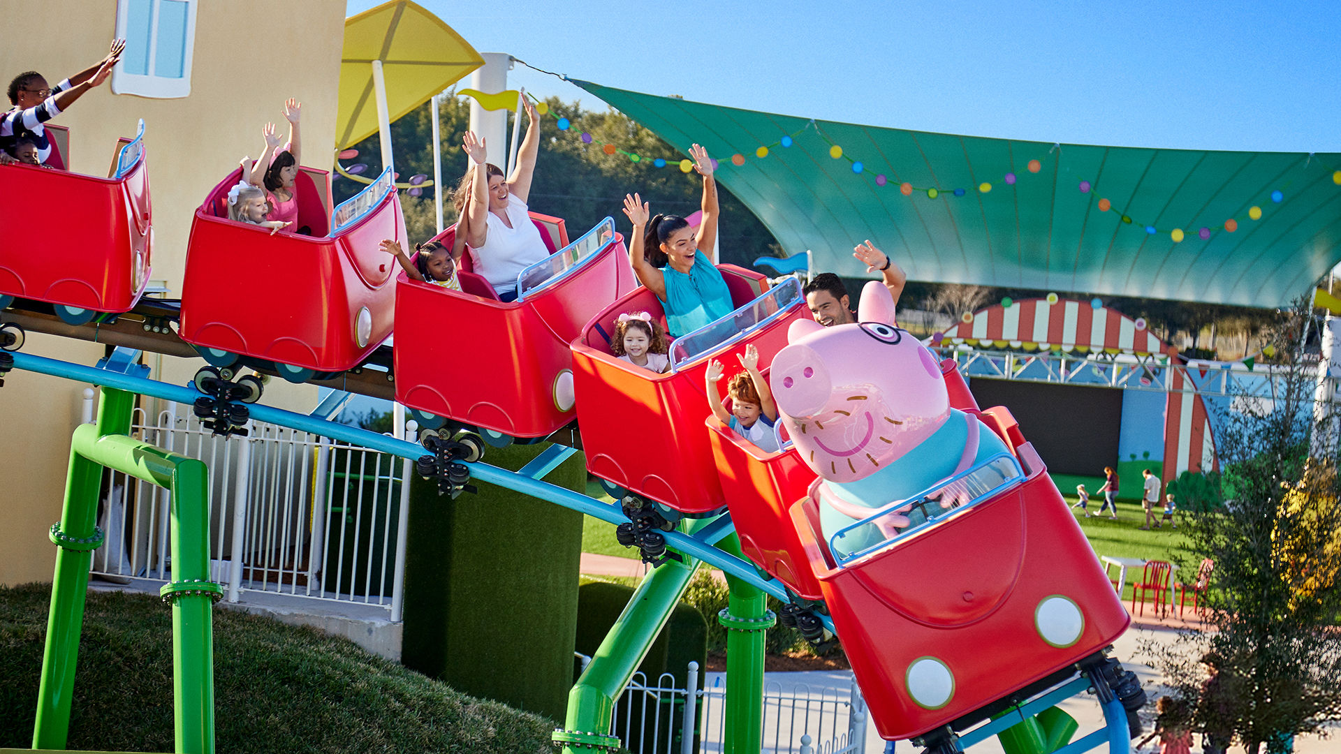 A train of red Peppa Pig cars cresting the track on Daddy Pig's Roller Coaster with riders' arms raised