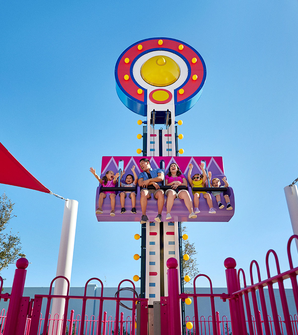 Families riding Mr. Bull's High Striker, a family drop tower with a purple and pink gondola and a bullseye target disc on top