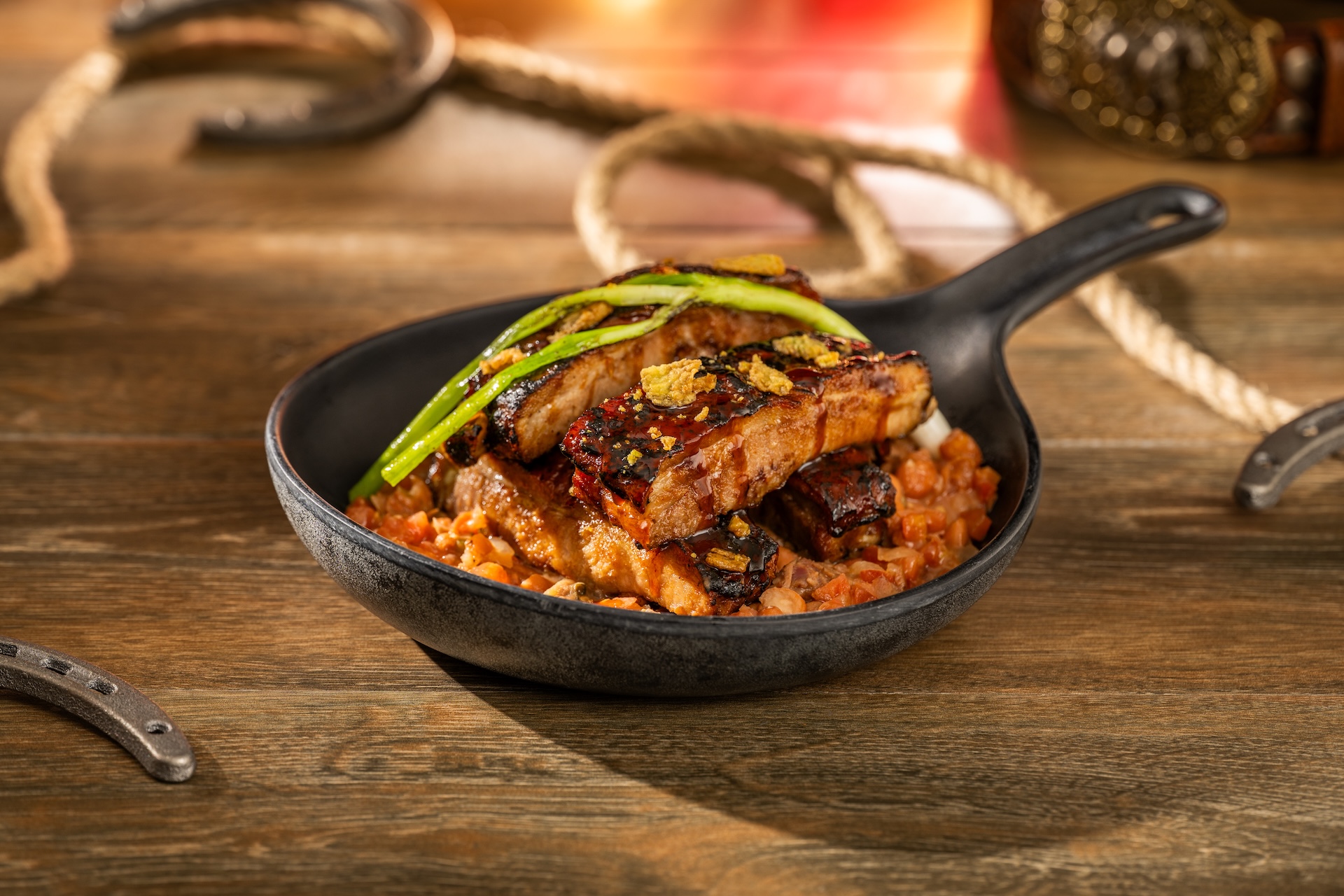 Glazed sticky ribs stacked in a small cast iron skillet over cowboy beans, topped with charred scallion and jalapeño crisps