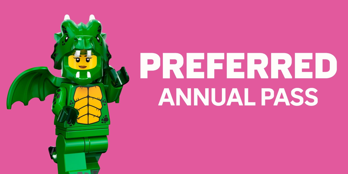 A wide promotional card on a hot pink background. At the left stands a LEGO minifigure wearing a full green dragon costume with a horned hood over its yellow smiling face, a large green bat wing spread behind its shoulder and a golden yellow scaled belly panel. At the right, in large white bold capitals, the word PREFERRED sits above the smaller words ANNUAL PASS.