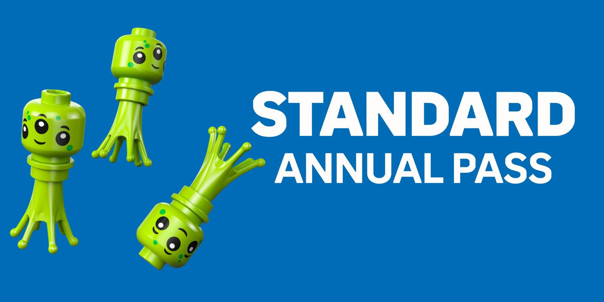 A wide promotional card on a flat mid blue background. Three lime green LEGO alien figures with rounded minifigure heads, large cartoon eyes, small smiles and tapered tentacle bodies float at different angles across the left half. At the right, in large white bold capitals, the word STANDARD sits above the smaller words ANNUAL PASS.