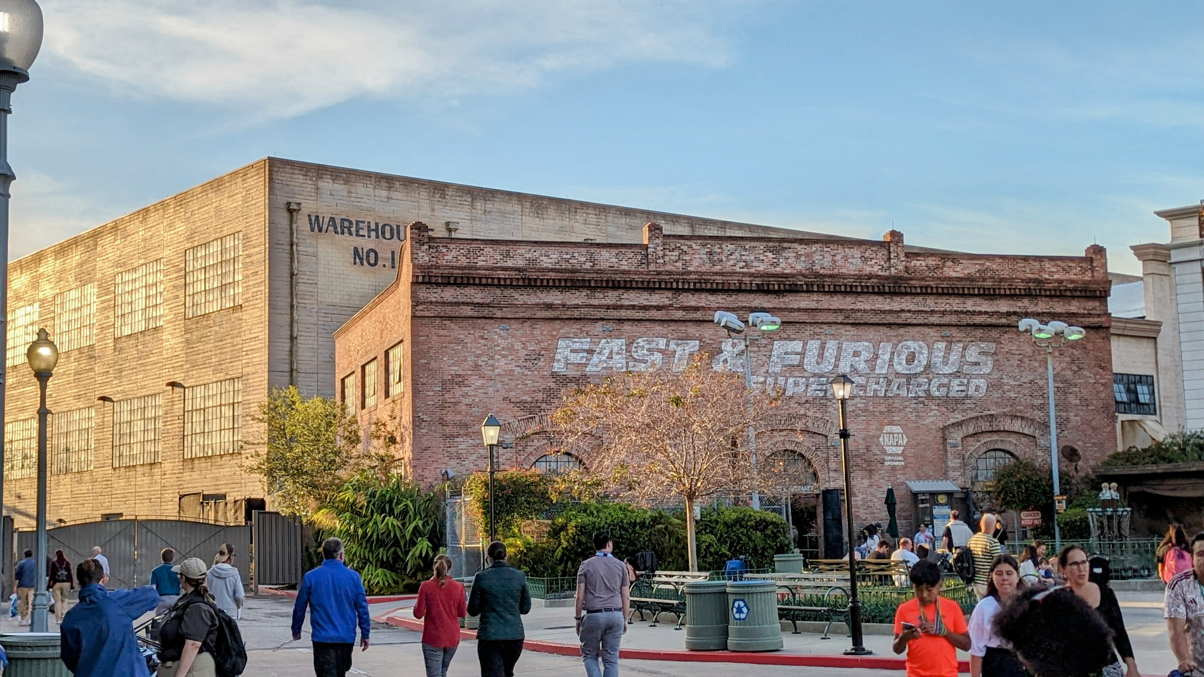 The red brick show building at golden hour with FAST & FURIOUS SUPERCHARGED painted large in white on its facade, WAREHOUSE NO. 1 lettered on the tan side wall, a NAPA sponsor sign beside the entrance arches and guests walking across the plaza