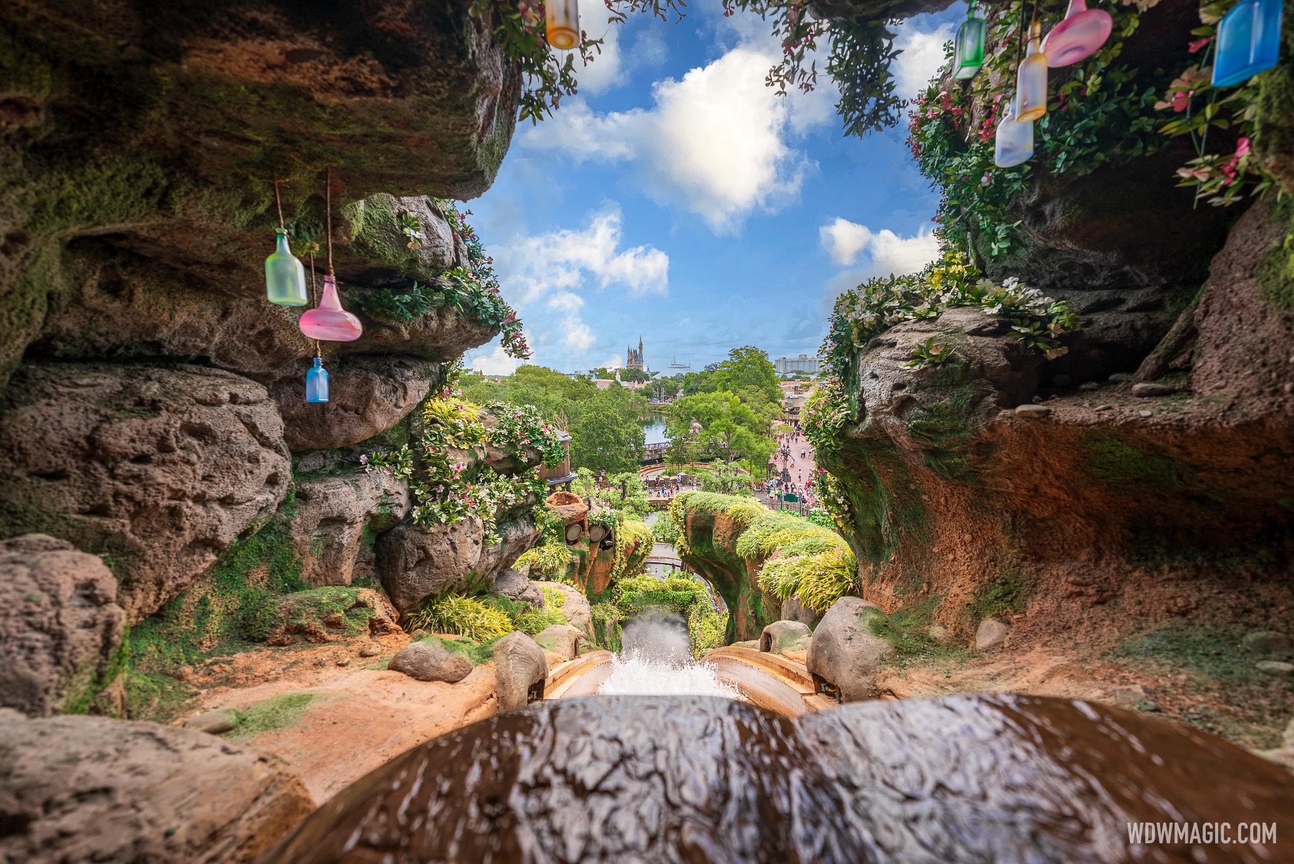 View from the top of the flume drop looking down the chute toward Frontierland, with hanging colored glass bottles in the rockwork and Cinderella Castle in the distance