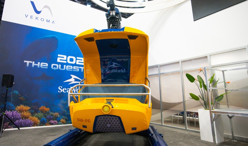 Head-on view of the yellow and blue SEAQuest submersible ride vehicle with its canopy open, a SeaWorld logo on the blue seatback inside and the overhead swing arm visible on top