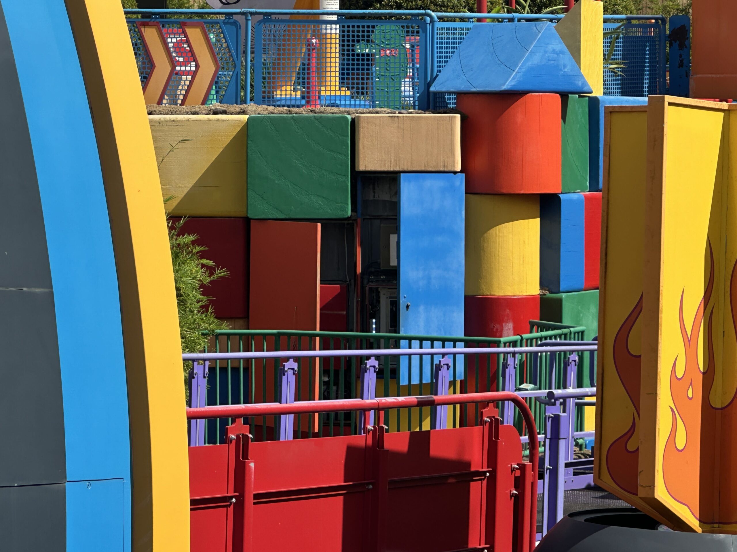 A blue access door swung open in the wall of oversized toy blocks at Slinky Dog Dash, exposing a recessed bay of grey electrical equipment and conduit behind green and purple railings.