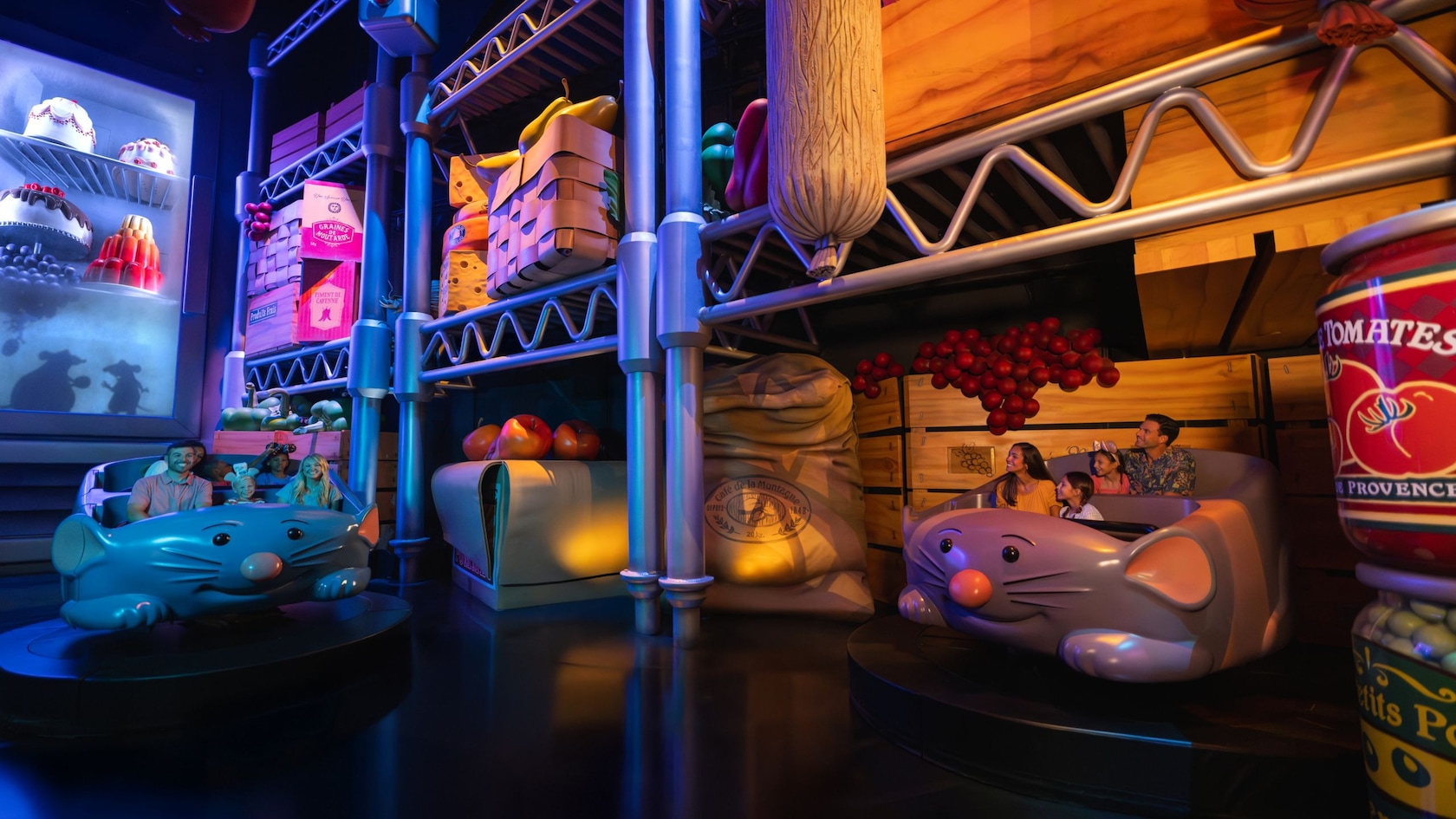 Two rat shaped ride vehicles carrying families through an oversized pantry set built at rat scale, with chrome shelving, a giant Tomates de Provence can at right, a large printed sack, a crate of tomatoes, and rat shadows on a frosted refrigerator door at far left