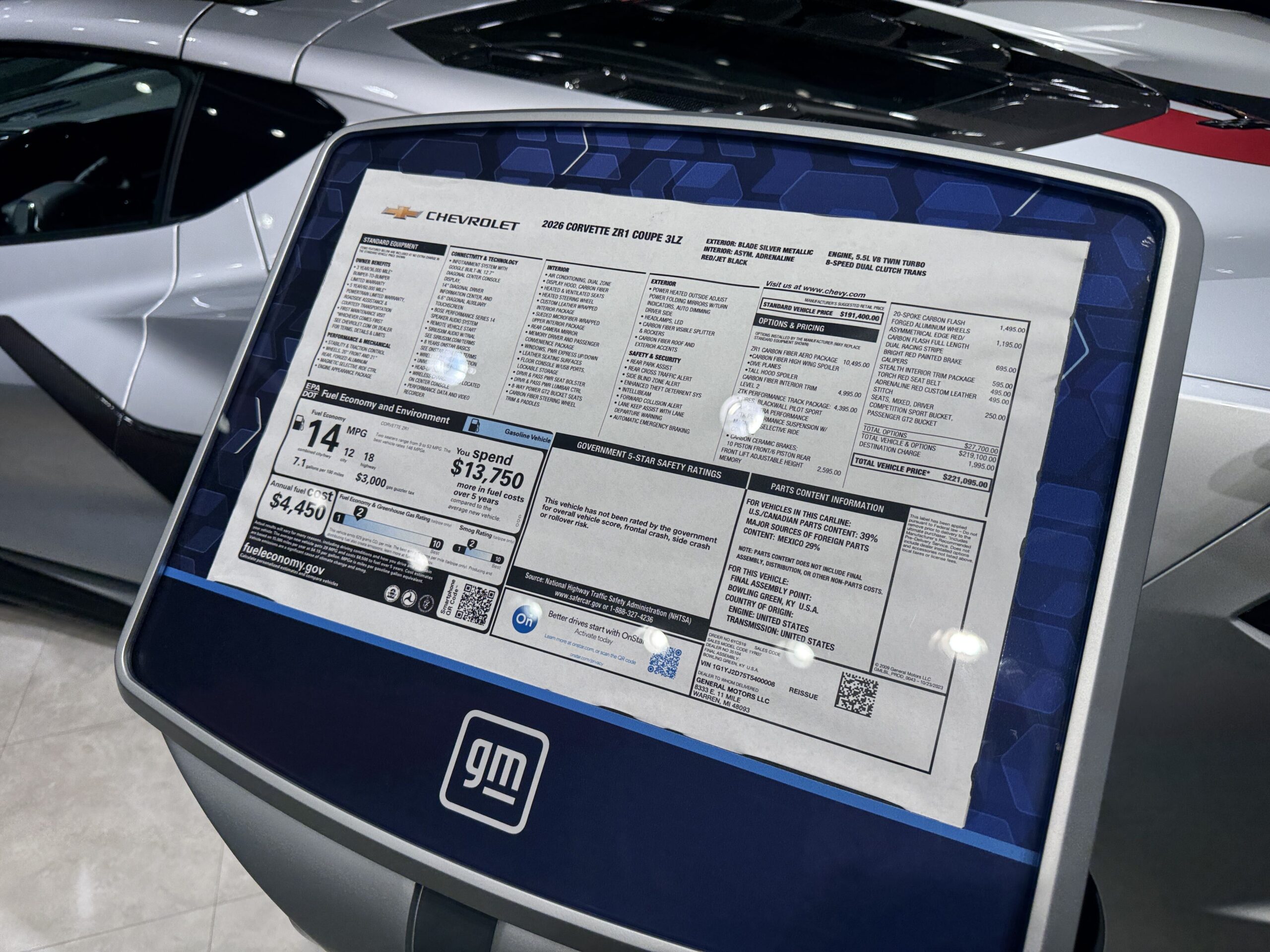 Close-up of the Monroney window sticker for a 2026 Corvette ZR1 Coupe 3LZ, showing the options and pricing panel and the EPA fuel economy panel, mounted on a stand with a GM logo.