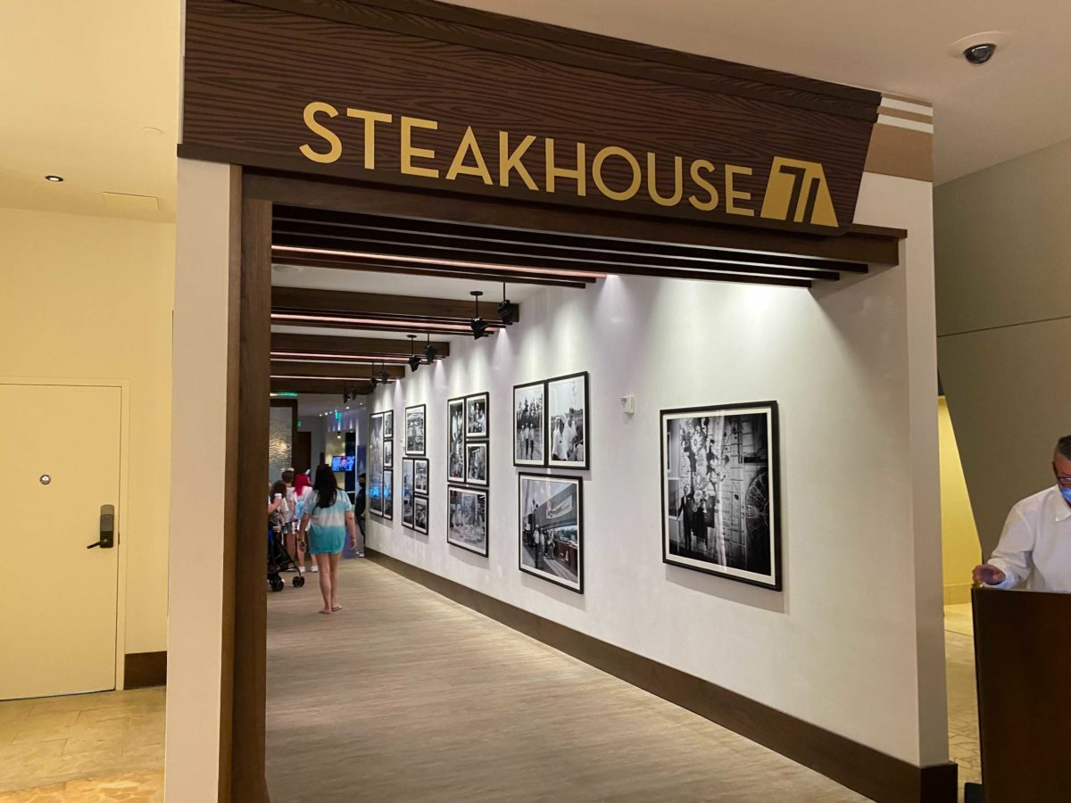 The entrance to Steakhouse 71, with a dark wood header carrying the restaurant name in gold letters and a gold badge around the numeral 71, opening onto a corridor hung with a grid of framed black and white historical Walt Disney World photographs.