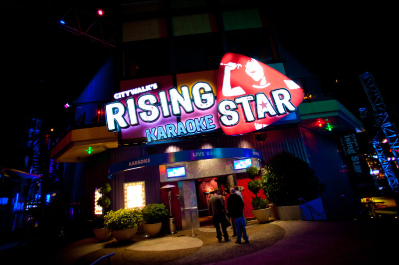 The exterior of CityWalks Rising Star karaoke club at night, with a large neon sign and a red logo showing a singer holding a microphone