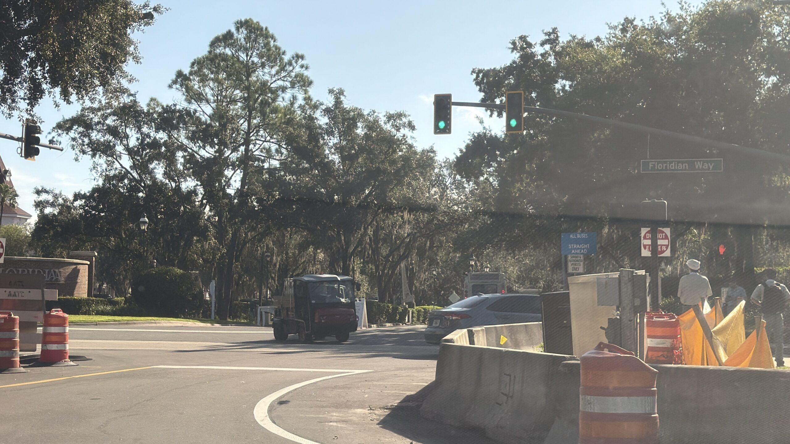 A traffic light with a Floridian Way street sign, a blue sign reading ALL BUSES STRAIGHT AHEAD above a smaller service vehicles placard, a Do Not Enter sign, concrete barriers and orange barrels