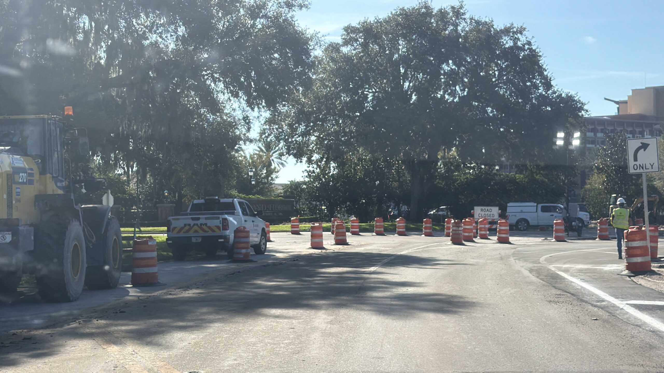 A line of orange construction barrels with a ROAD CLOSED sign across a road, the Grand Floridian monument sign behind them, a yellow front loader at left and a right turn only sign at right