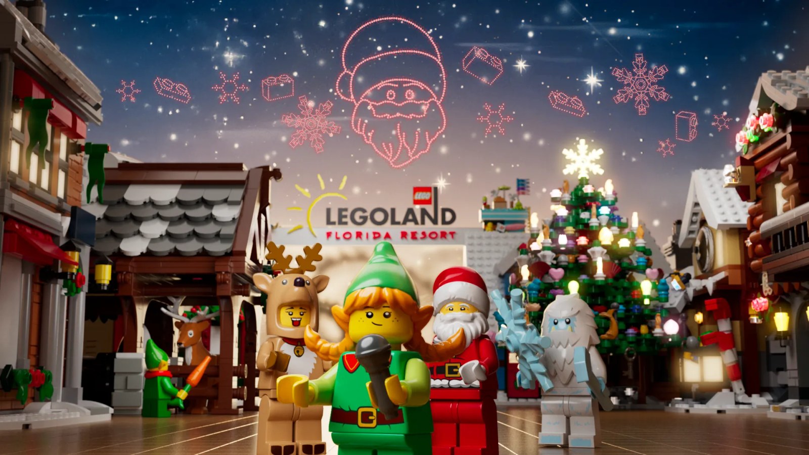Key art for LEGOLAND Christmas Bricktacular showing LEGO minifigure characters including an elf holding a microphone, Santa, a child in a reindeer costume and a yeti, in front of a lit LEGO Christmas tree with a red drone show Santa face in the night sky
