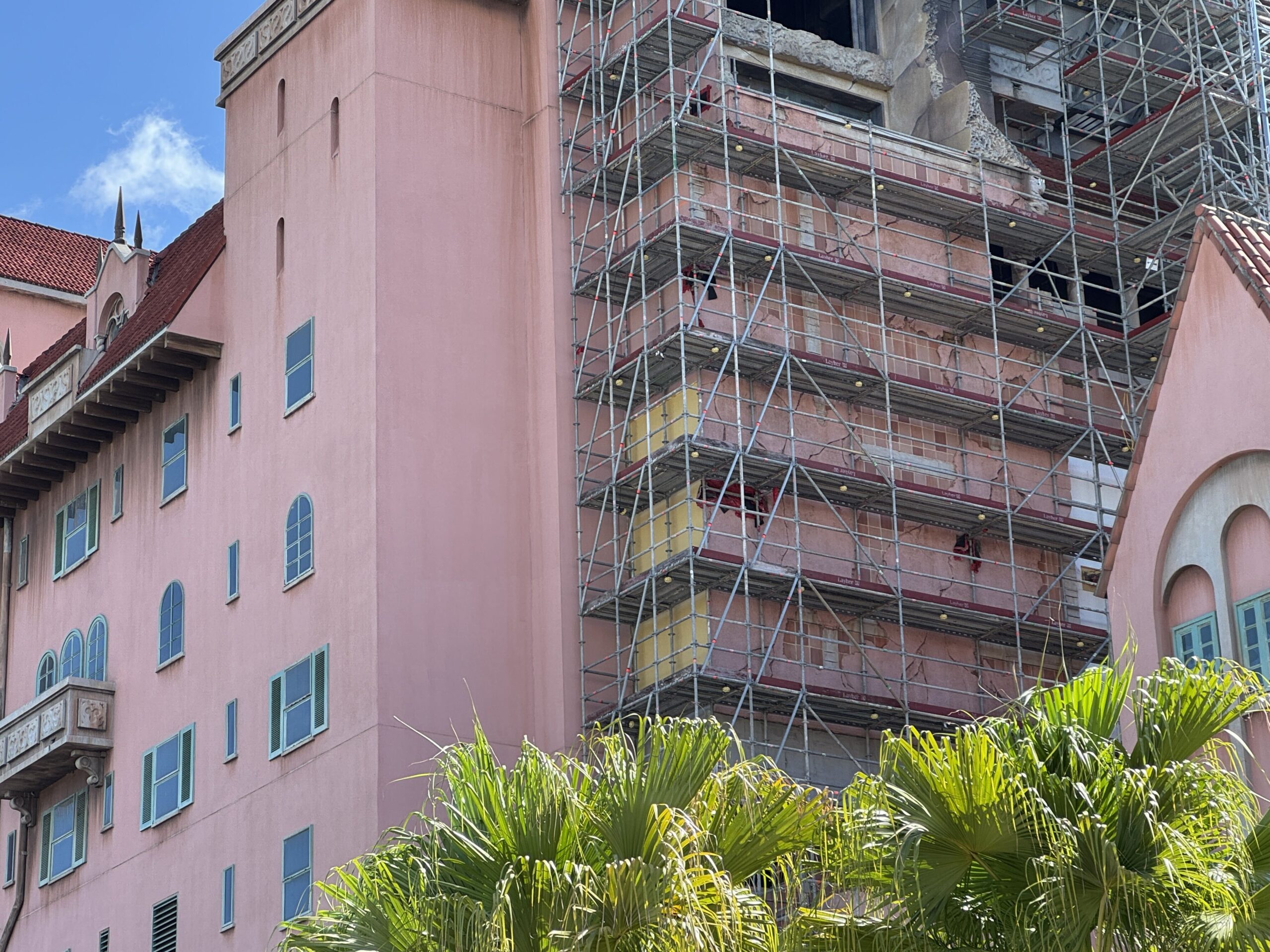 Close up of the edge of the scaffolding on the Tower of Terror, with a smooth pink wall at left and, behind the scaffolding at right, aged, weathered wall sections, yellow patches and red plastic around several openings