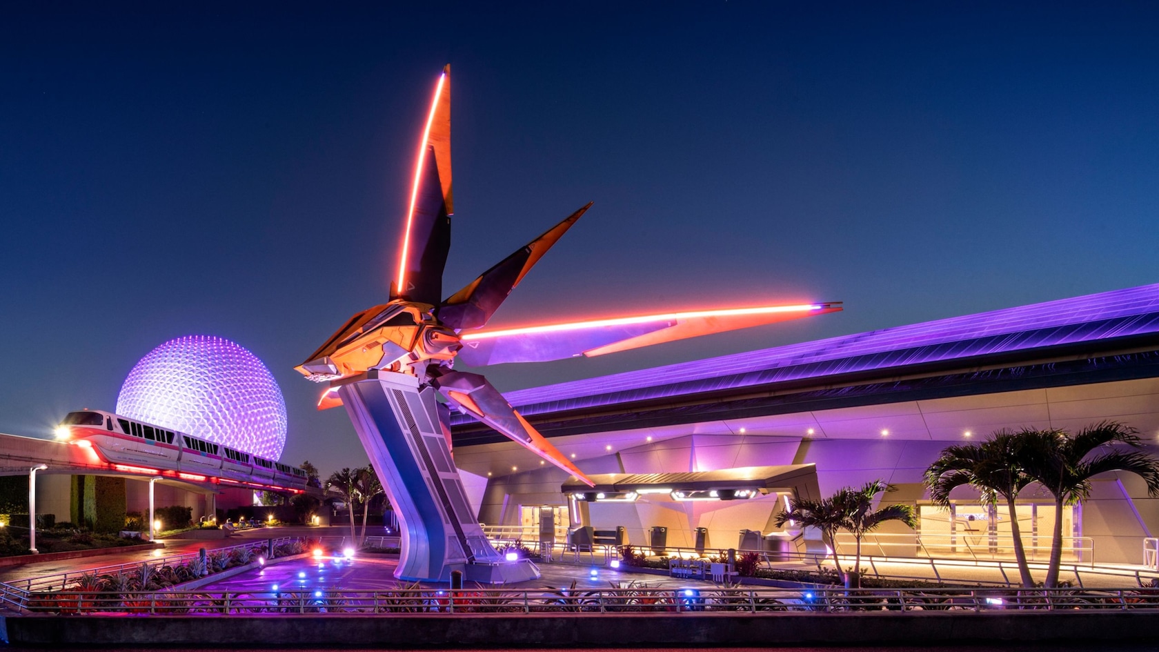 The Guardians of the Galaxy: Cosmic Rewind building at dusk, with a tall starship sculpture lit with orange lines out front, a monorail passing on the left and Spaceship Earth glowing purple behind it