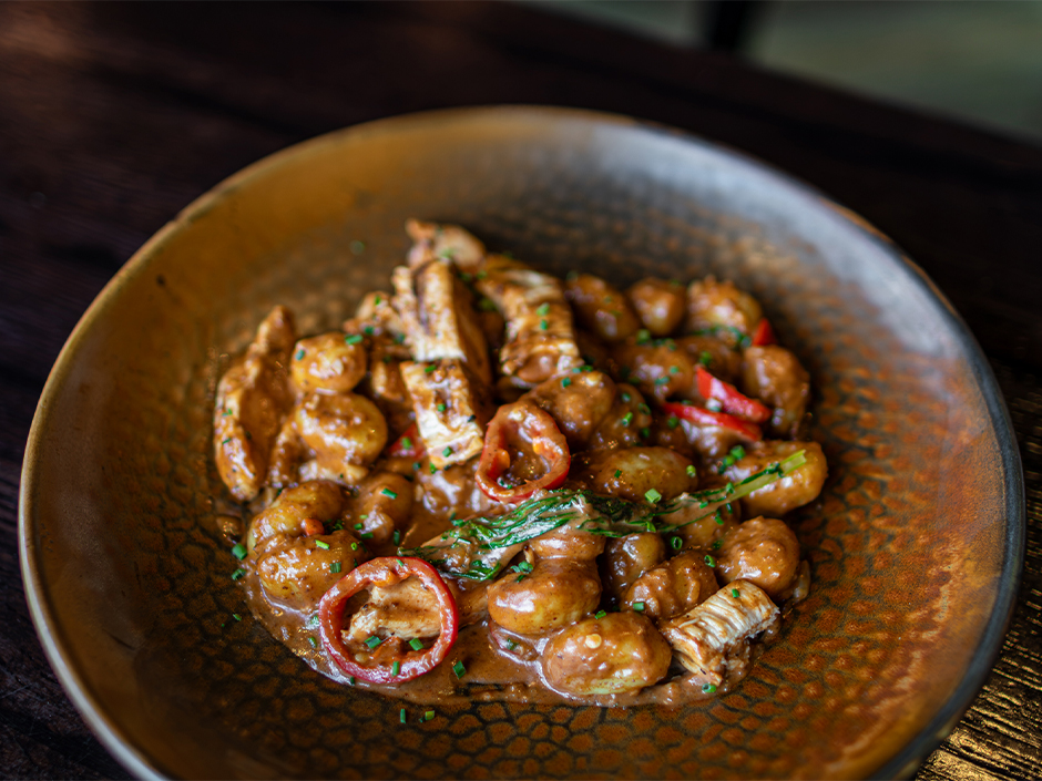 A bowl of gnocchi with grilled chicken, sweet peppers and rapini in a mole cream sauce