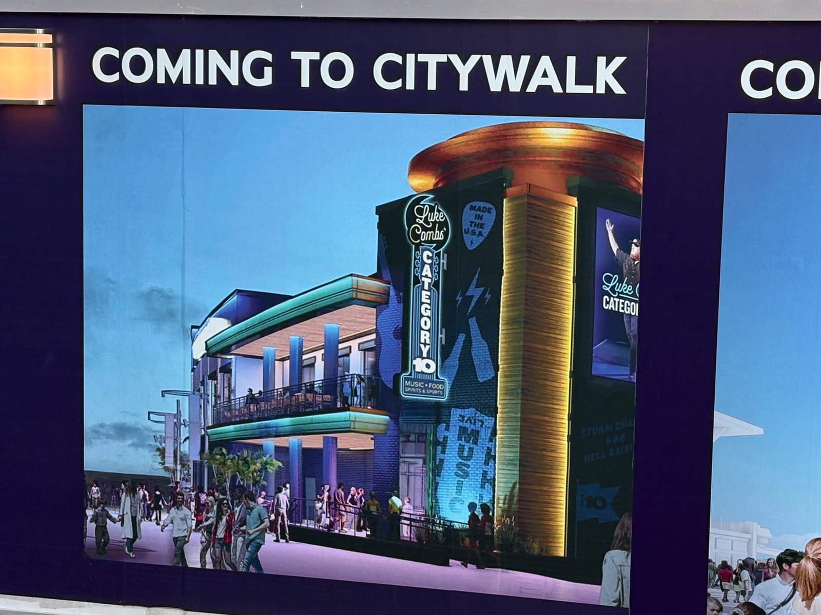 A construction wall panel reading Coming to CityWalk showing a dusk rendering of a building with a round gold-lit roof cap, a vertical Luke Combs Category 10 sign and a covered balcony with diners