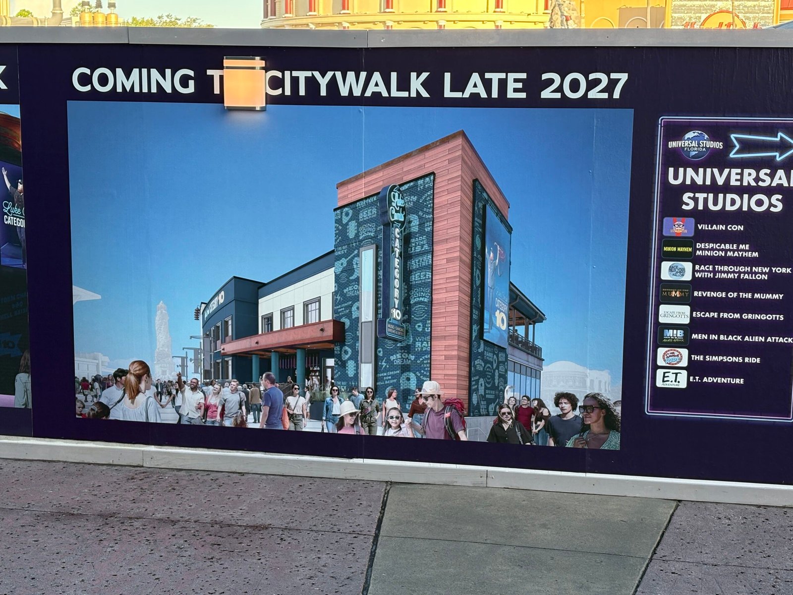 A CityWalk construction wall panel reading Coming to CityWalk Late 2027 over a daytime rendering of a building with a red corner tower and a vertical Category 10 sign, next to a Universal Studios attraction list