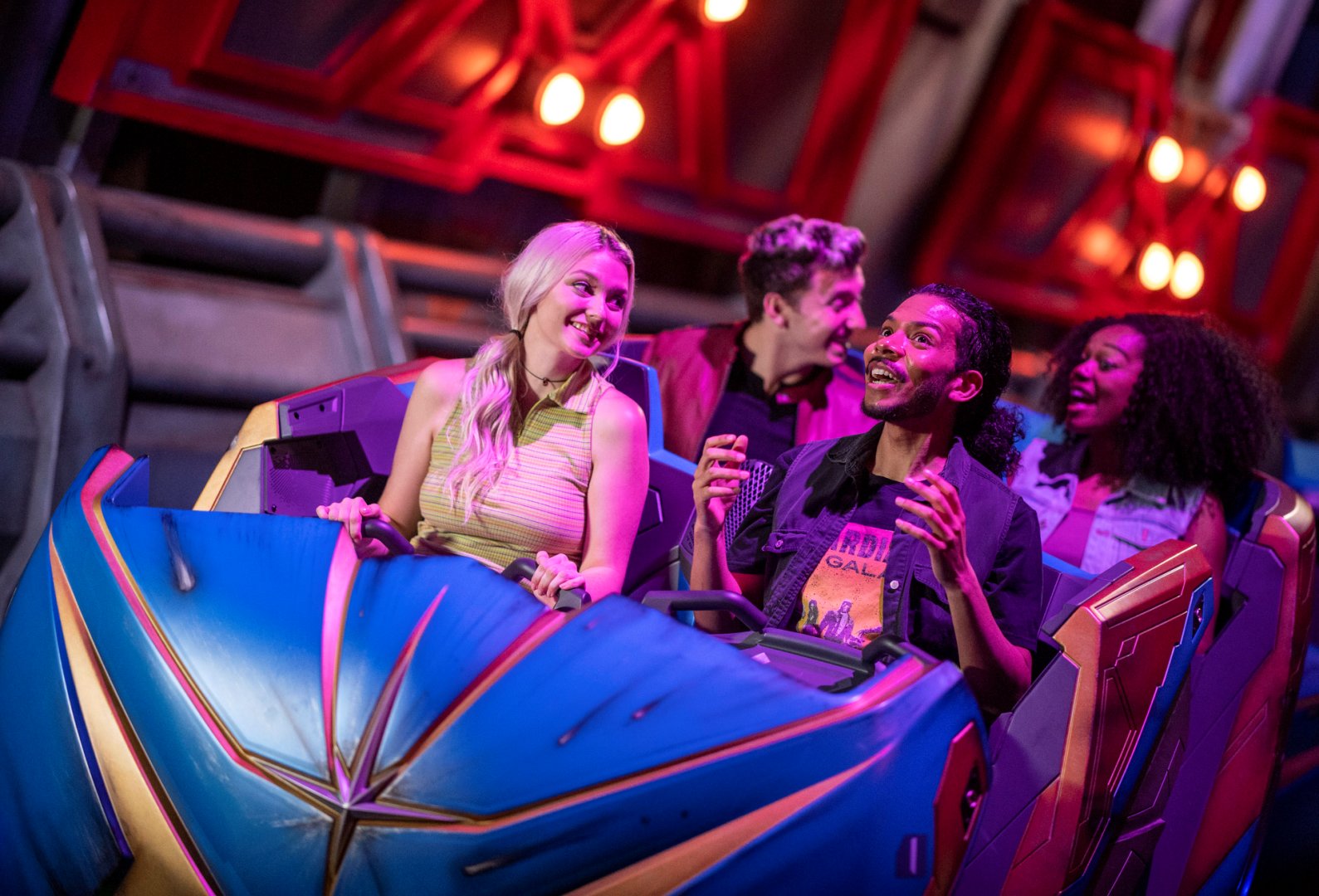 Four smiling riders in a blue and gold ride vehicle under red lights inside Guardians of the Galaxy: Cosmic Rewind