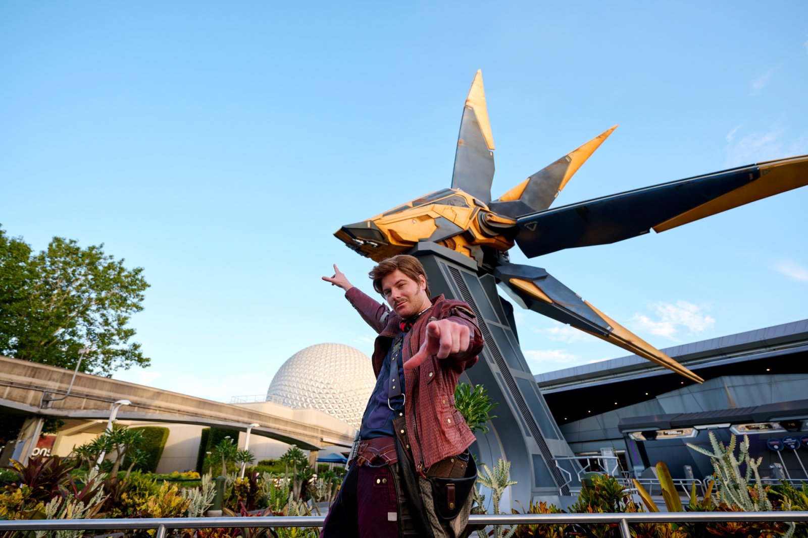 Star-Lord in a red leather jacket points at the camera in front of the starblaster sculpture outside Cosmic Rewind, with Spaceship Earth in the background