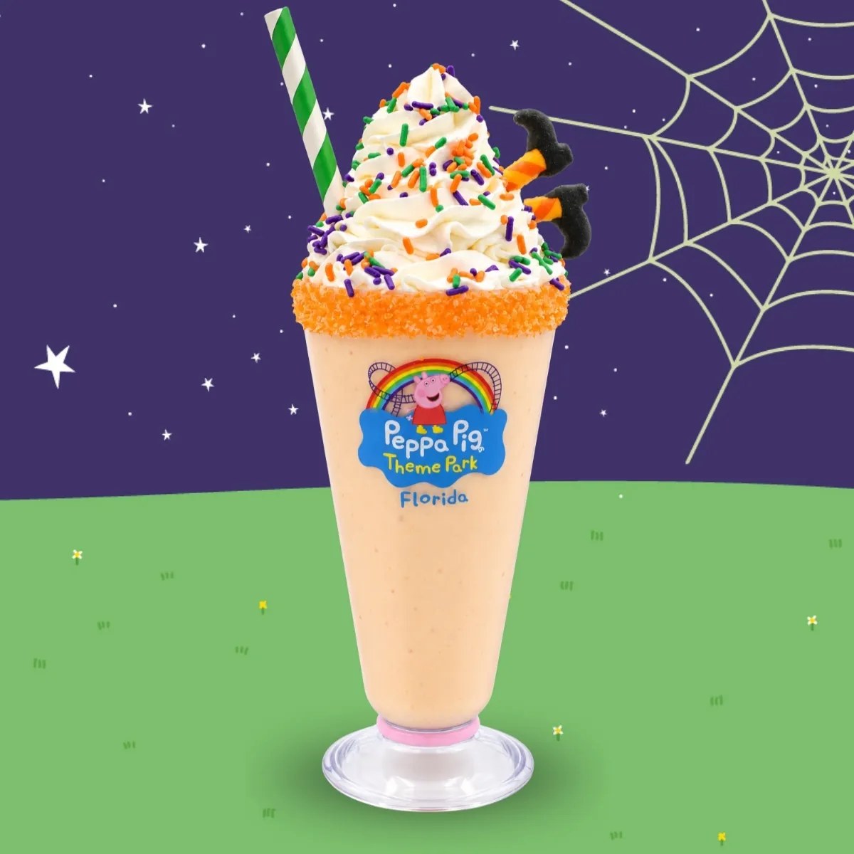 An orange milkshake in a Peppa Pig Theme Park Florida cup with an orange sugar rim, whipped cream, orange, green and purple sprinkles, a green striped straw and icing witch feet, against a starry sky and spider web