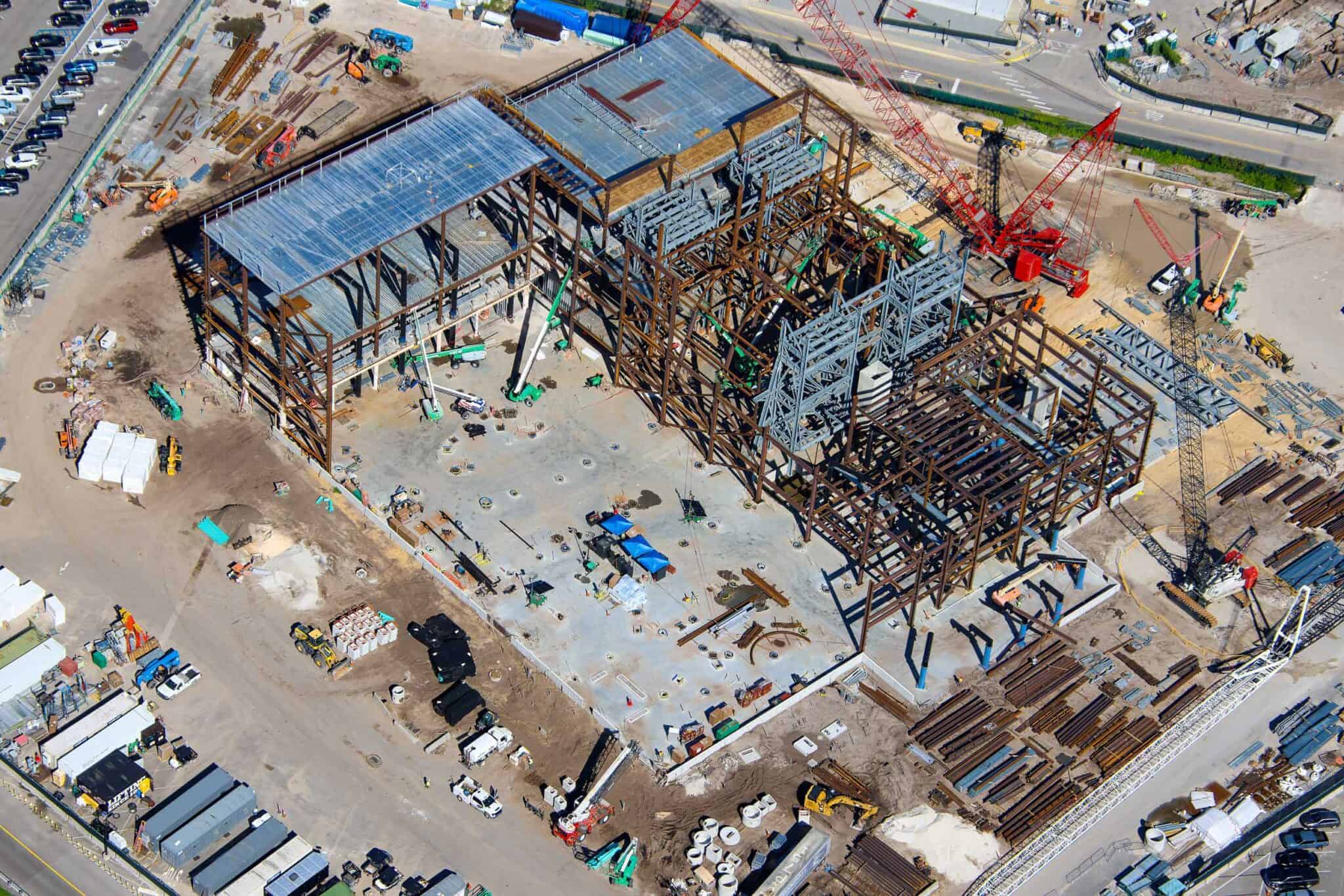 Overhead view of the Monsters, Inc. coaster show building under construction, with metal roof decking over bays at one end and a large open concrete slab in the foreground