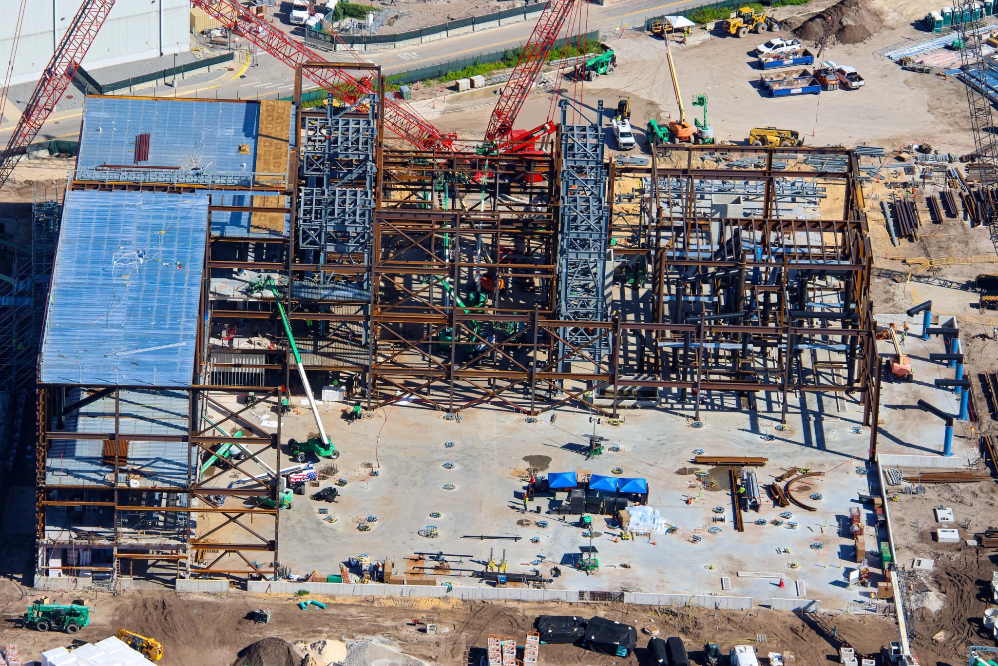 Closer overhead view showing metal decking and plywood over the left bays, light gray painted steel columns in the center, and low pale concrete block work among the rust colored framing at right