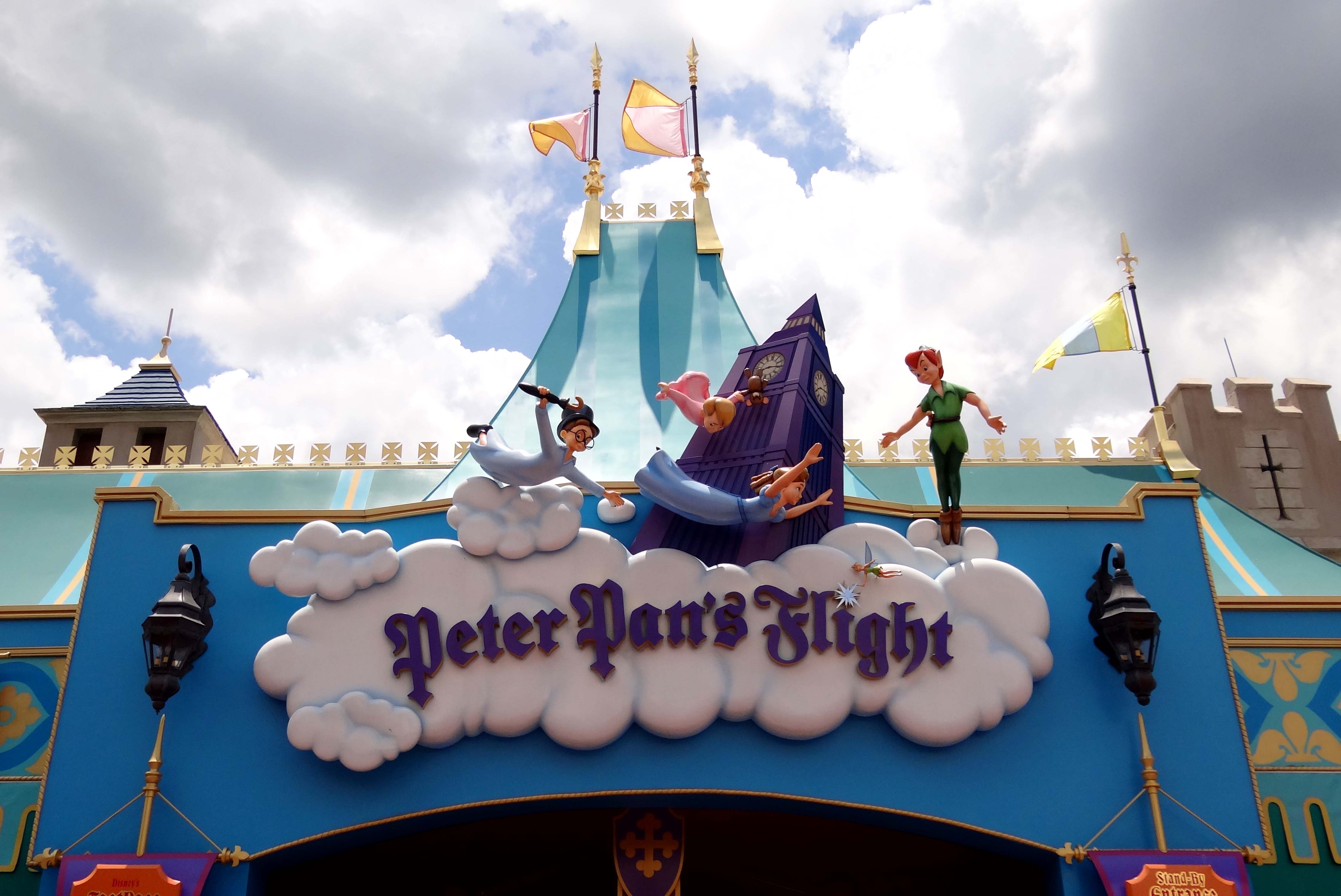 The Peter Pan's Flight marquee, a white cloud-shaped sign with the ride name in purple script, with figures of Wendy, John and Michael flying past a purple Big Ben clock tower and Peter Pan in green standing at the right end of the sign