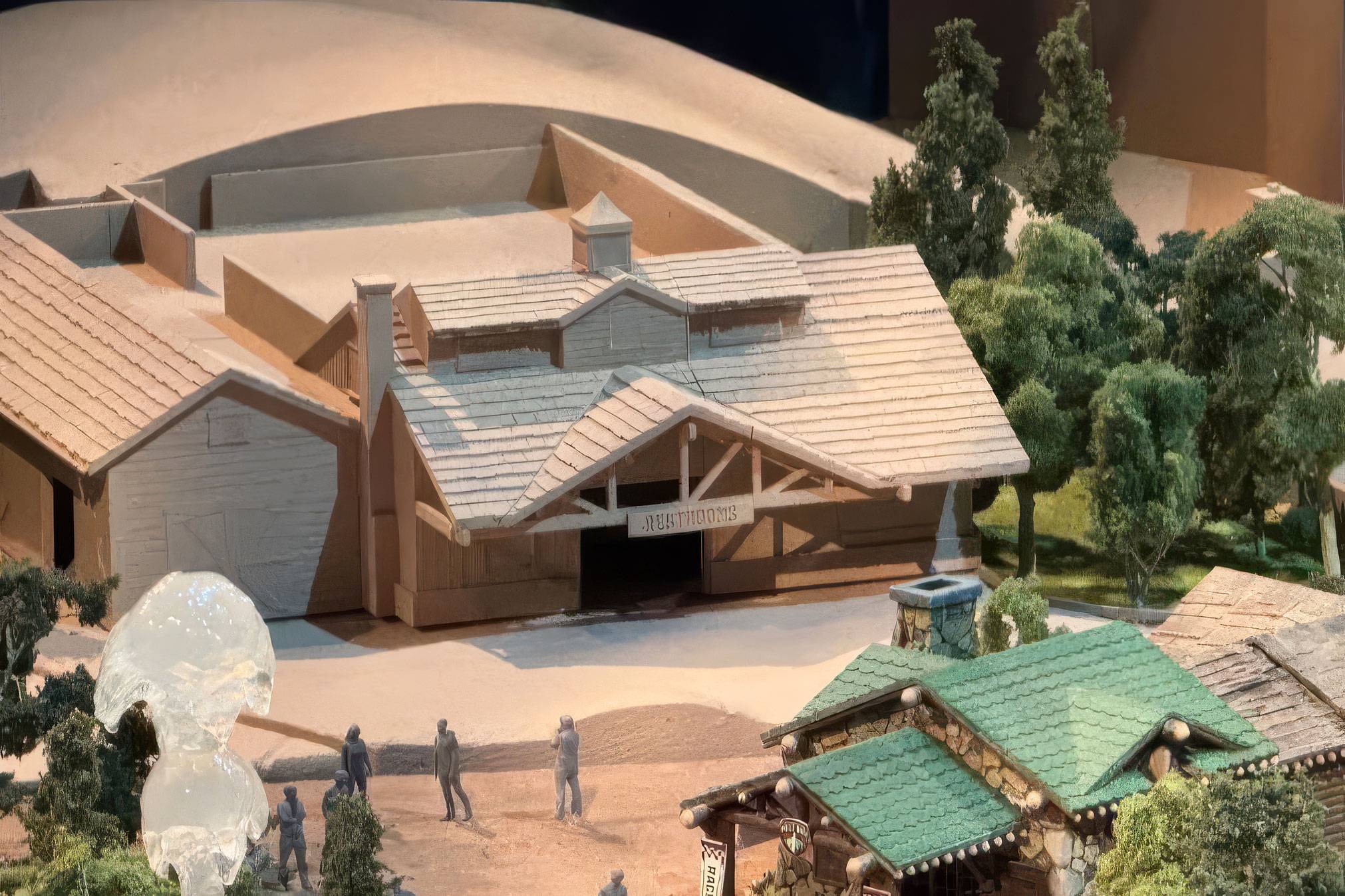 Close view of the Piston Peak scale model showing the small lodge style building, with a sign hung beneath its timber covered entry porch and model figures standing on the path in front