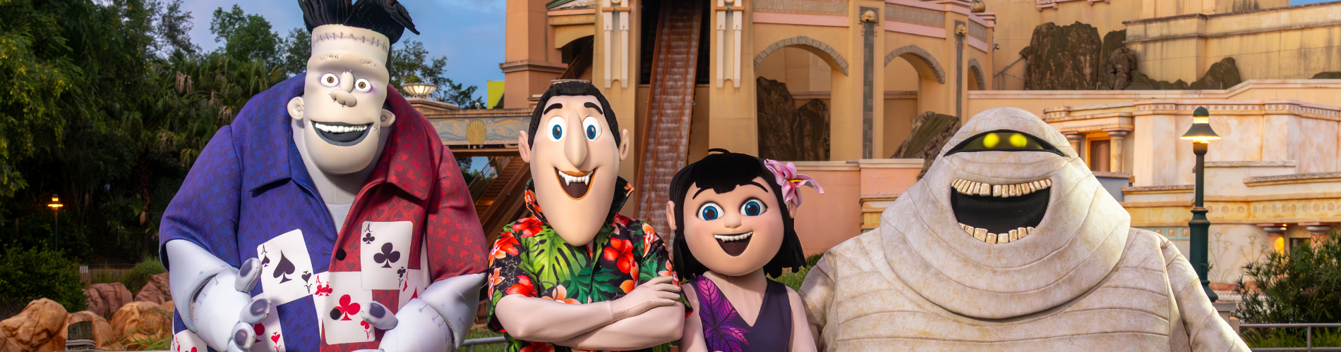 Costumed Hotel Transylvania characters Frank, Dracula, Mavis and Murray the mummy posed together in front of a SeaWorld building at dusk