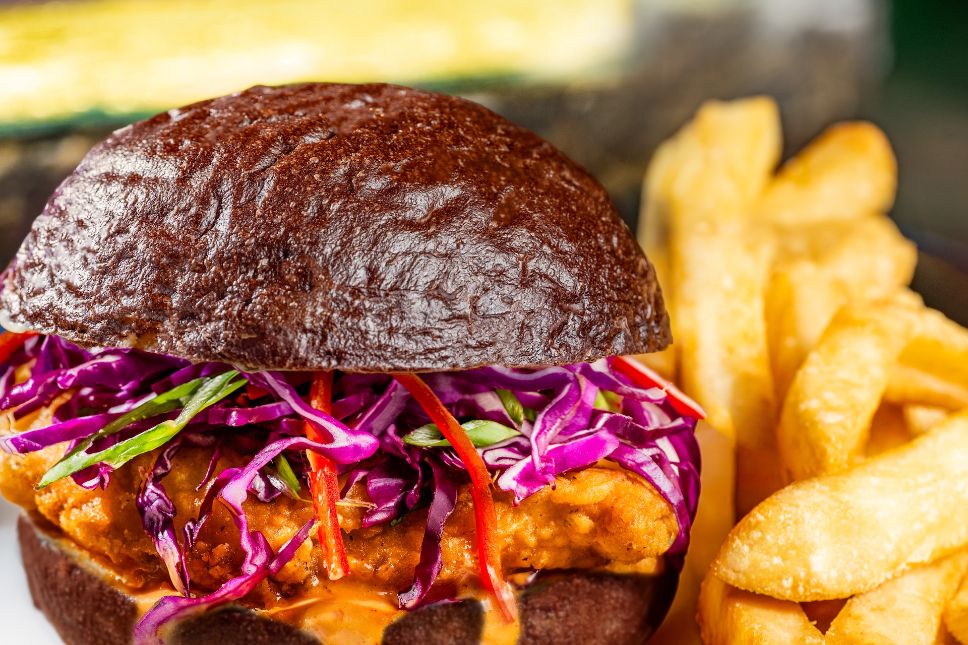Devilish Crispy Chicken Sandwich on a black kaiser roll with red cabbage and Fresno peppers, served with french fries