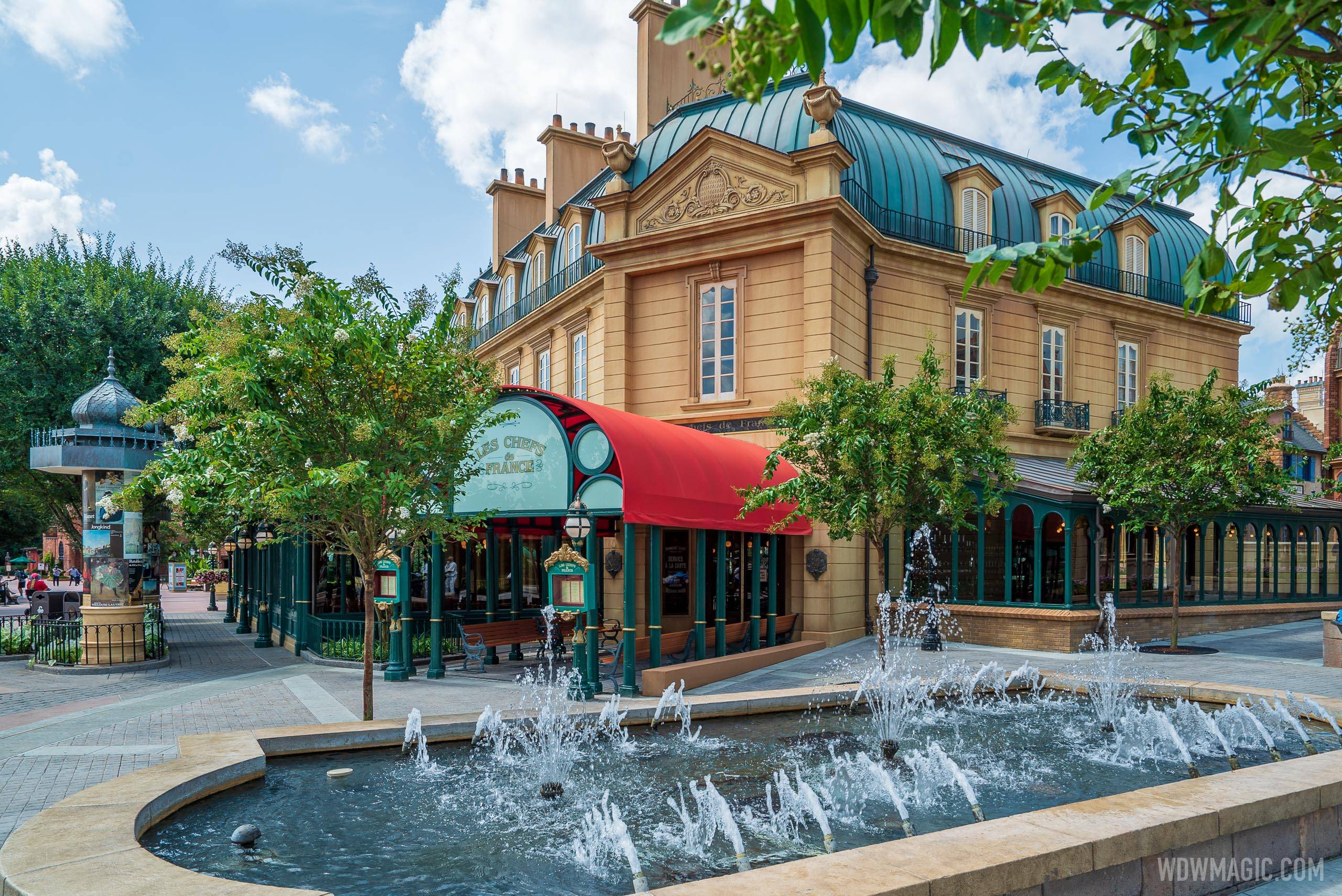 The tan French-style building housing Chefs de France with its green mansard roof and chimneys, a red awning over the restaurant entrance and a fountain splashing in the foreground