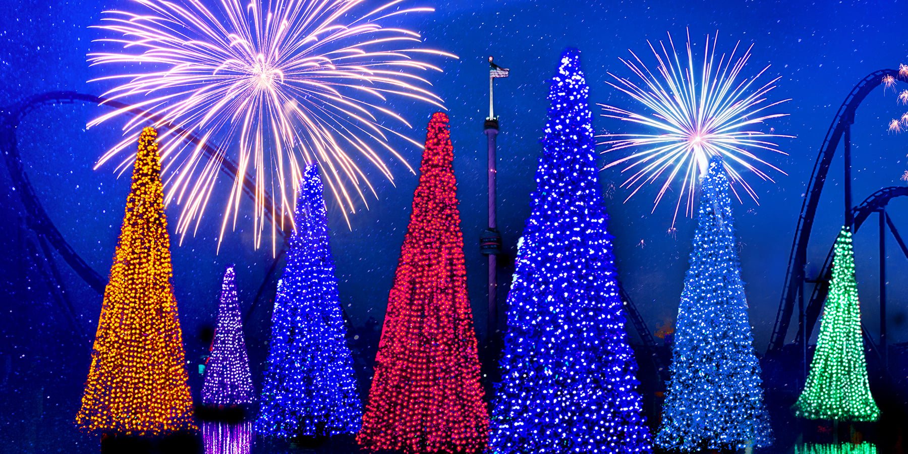 SeaWorld Christmas Celebration promotional image of the Sea of Trees, tall cone-shaped trees lit in gold, purple, blue, red and green, under fireworks and a snowy night sky, with roller coaster track silhouetted behind