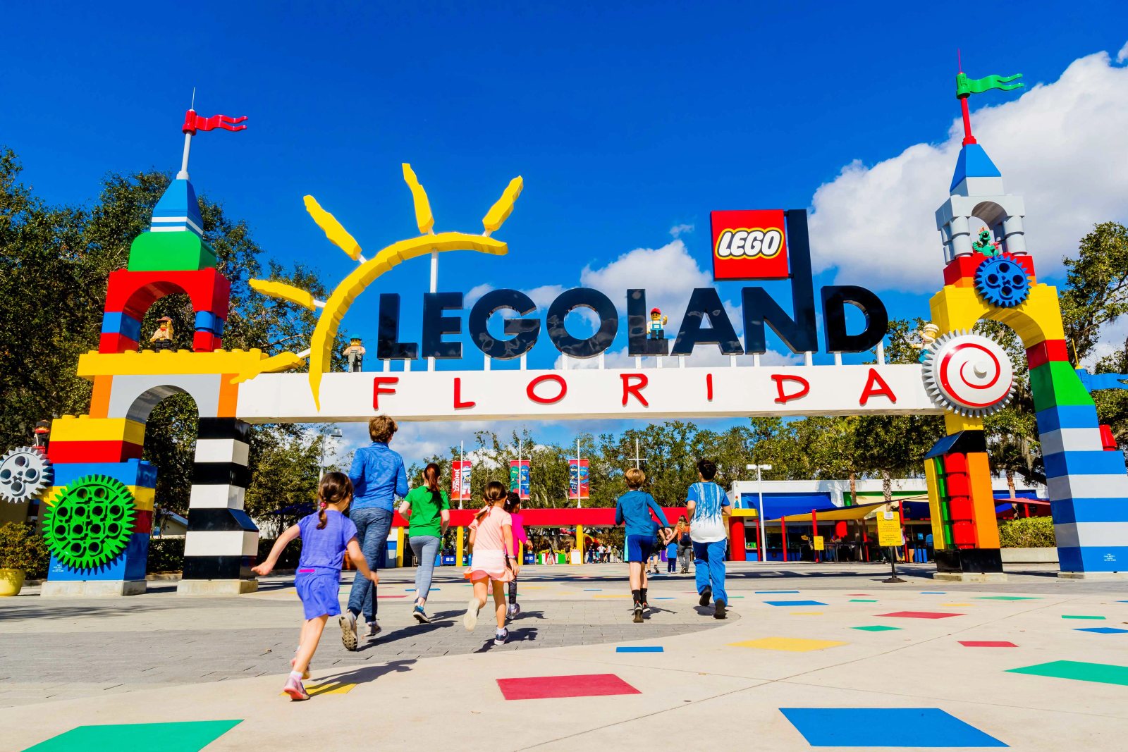 Children run toward the colorful LEGOLAND Florida entrance arch under a blue sky