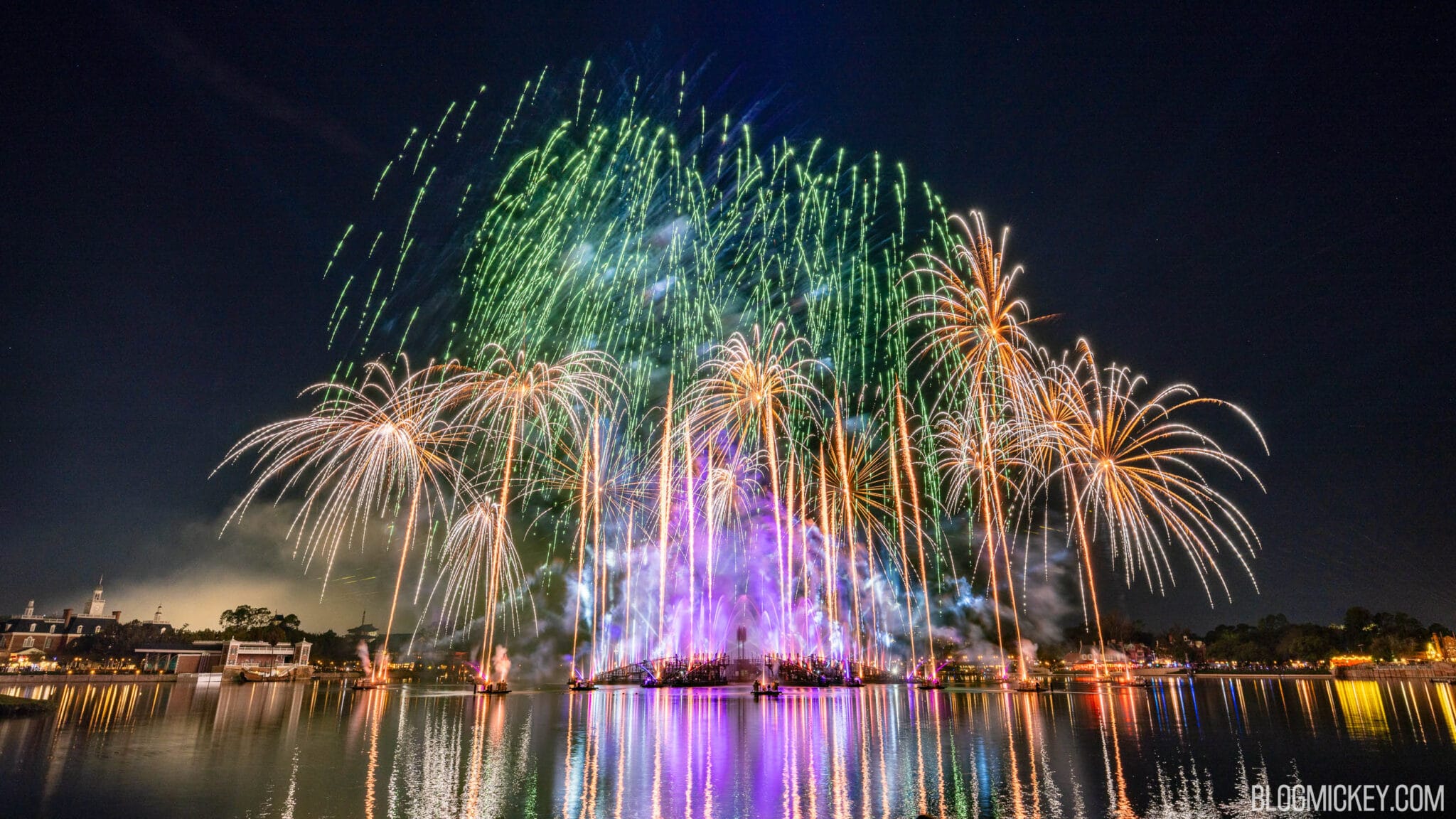 Gold and green fireworks burst over World Showcase Lagoon at EPCOT during Luminous: The Symphony of Us, with purple-lit fountains and barges on the water and the American Adventure pavilion at left