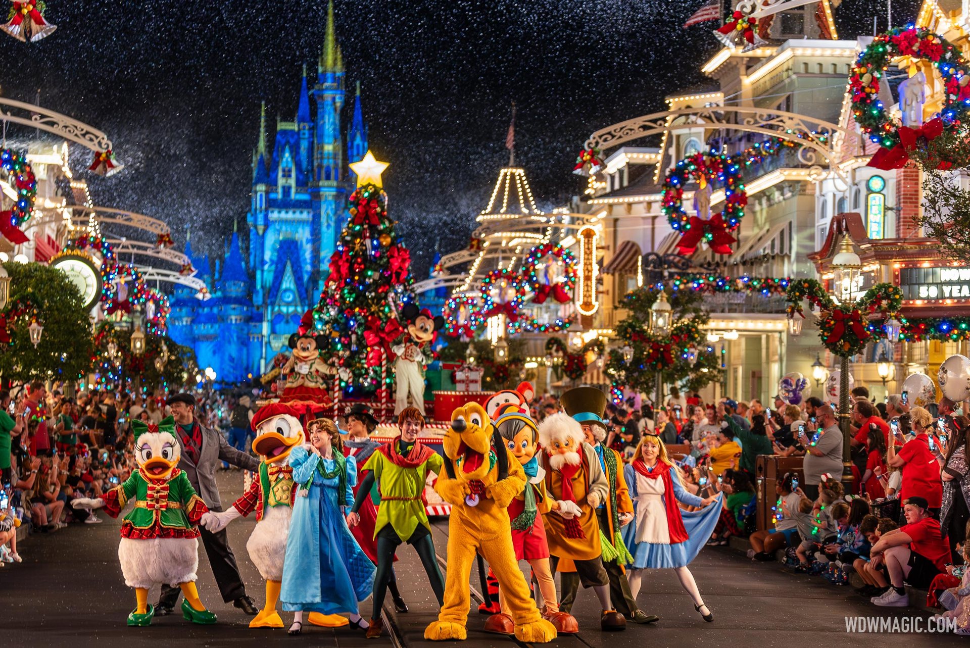 Daisy Duck, Donald Duck, Pluto and other Disney characters dance along a light-strung Main Street, U.S.A. under falling snow, ahead of a Christmas tree float and a blue-lit Cinderella Castle, as crowds watch