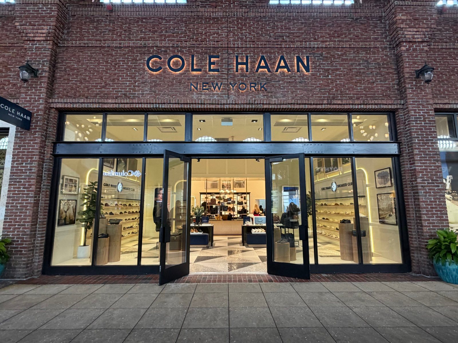 Brick storefront with COLE HAAN NEW YORK lettering above open glass doors, with shoe displays visible inside