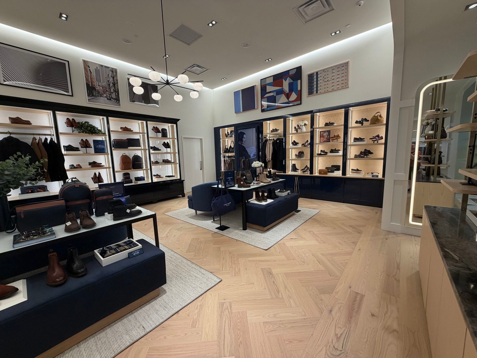 Store interior with lit wall shelves of shoes and bags, navy benches with white display tables and a herringbone wood floor